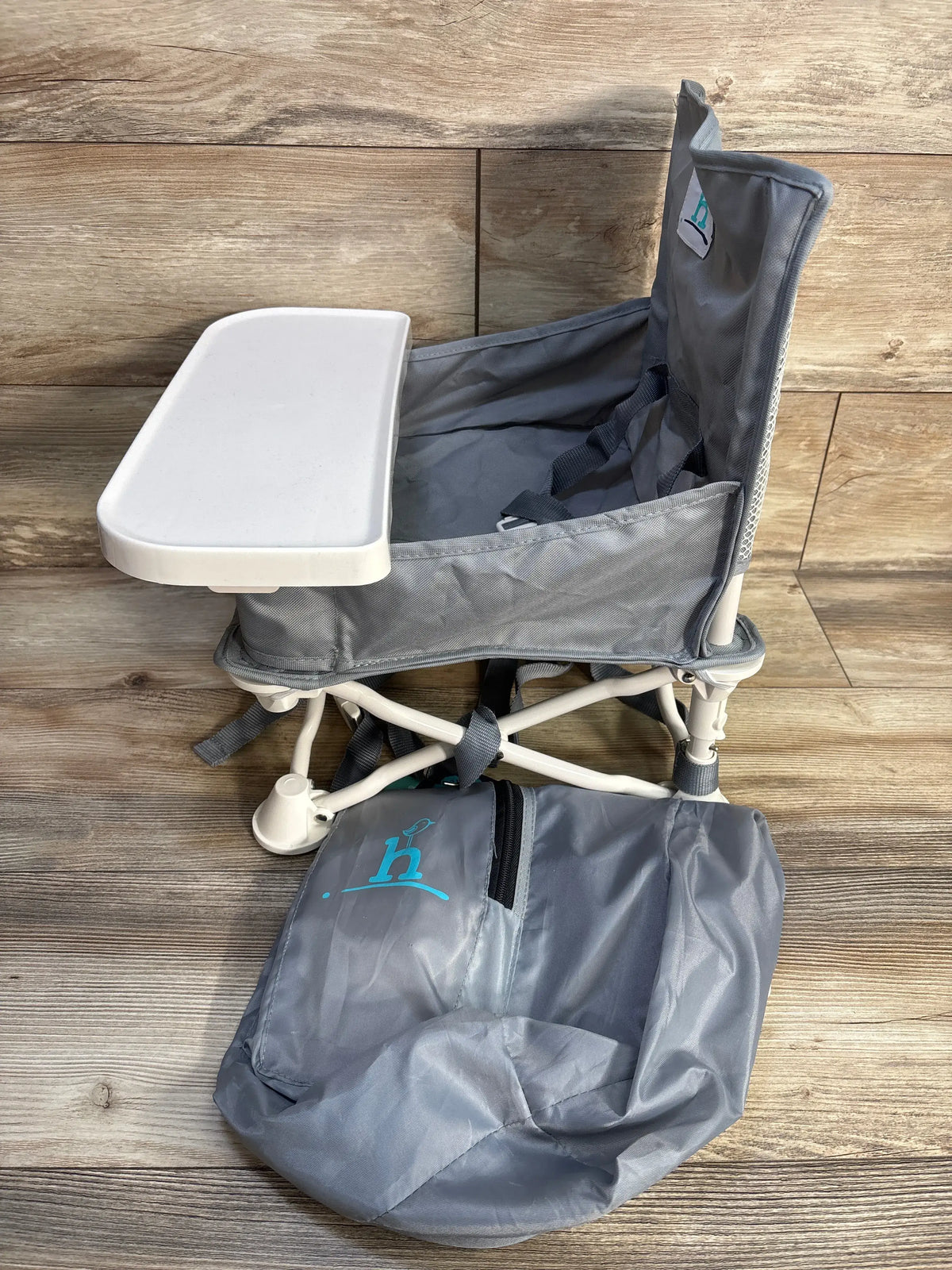 Front view of Hiccapop OmniBoost folding booster chair in gray showcasing white tray, safety harness, and carry bag