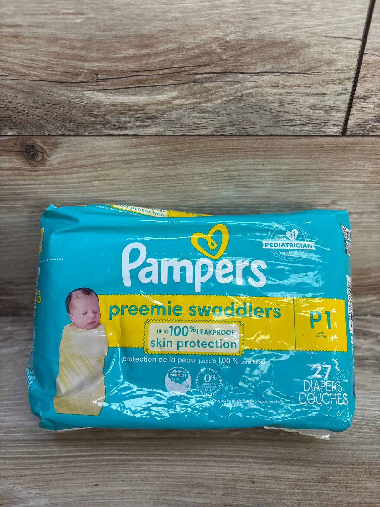 Front view of Pampers Preemie Swaddlers pack with up to 100 percent leakproof skin protection claim, size P1 27ct on wood