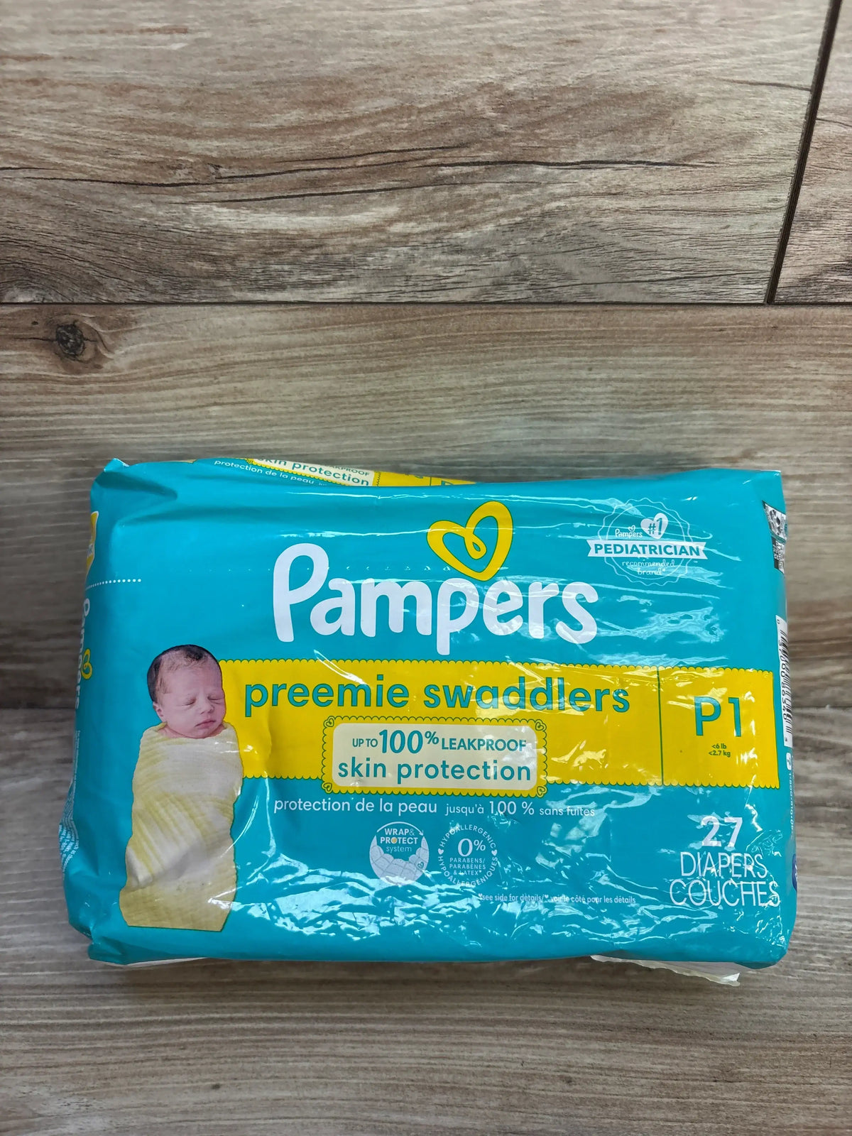 Front view of Pampers Preemie Swaddlers pack with up to 100 percent leakproof skin protection claim, size P1 27ct on wood