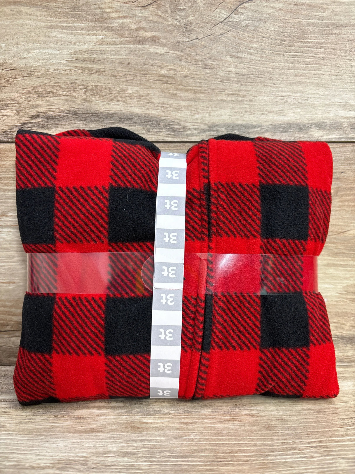 Red and black plaid fleece blanket size 3T folded with size label on wooden background