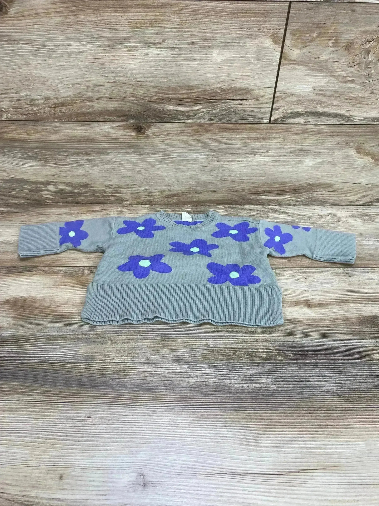 Flat lay of Baby Gap knit sweater in sage green with purple floral print and split scalloped hem on wood plank floor