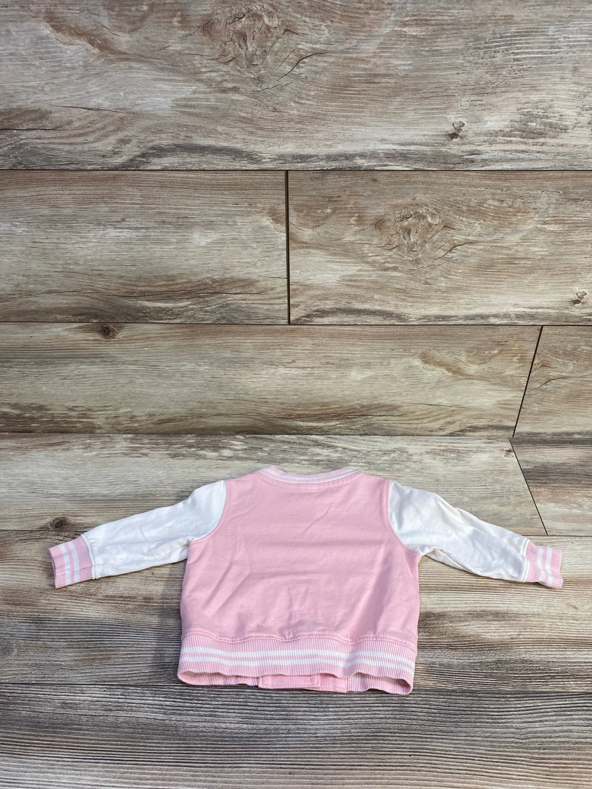 Back view of Carter’s pink varsity jacket showcasing white sleeves and striped ribbed trim on a wood-grain background