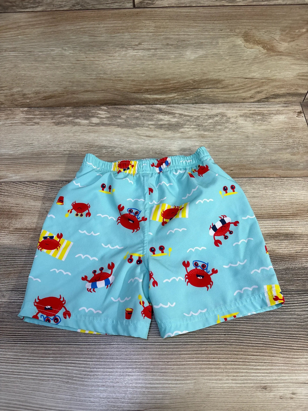 Front view of Banana Boat swim trunks, seafoam crab print, size 24M, with elastic waist on wood-grain background