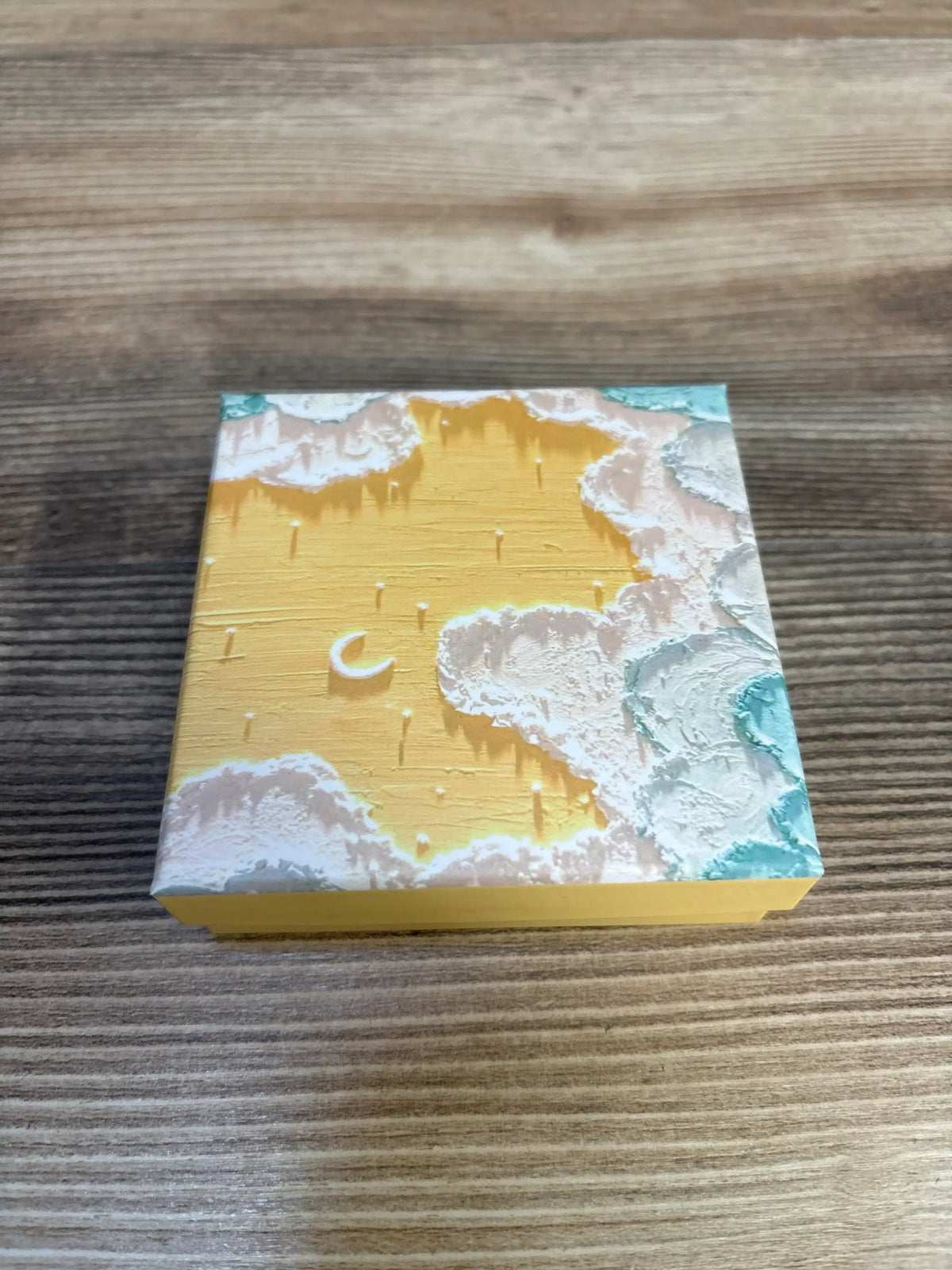 Three-quarter view of new Pregnancy Affirmation Cards box in yellow with textured cloud and crescent moon lid design on wood plank floor