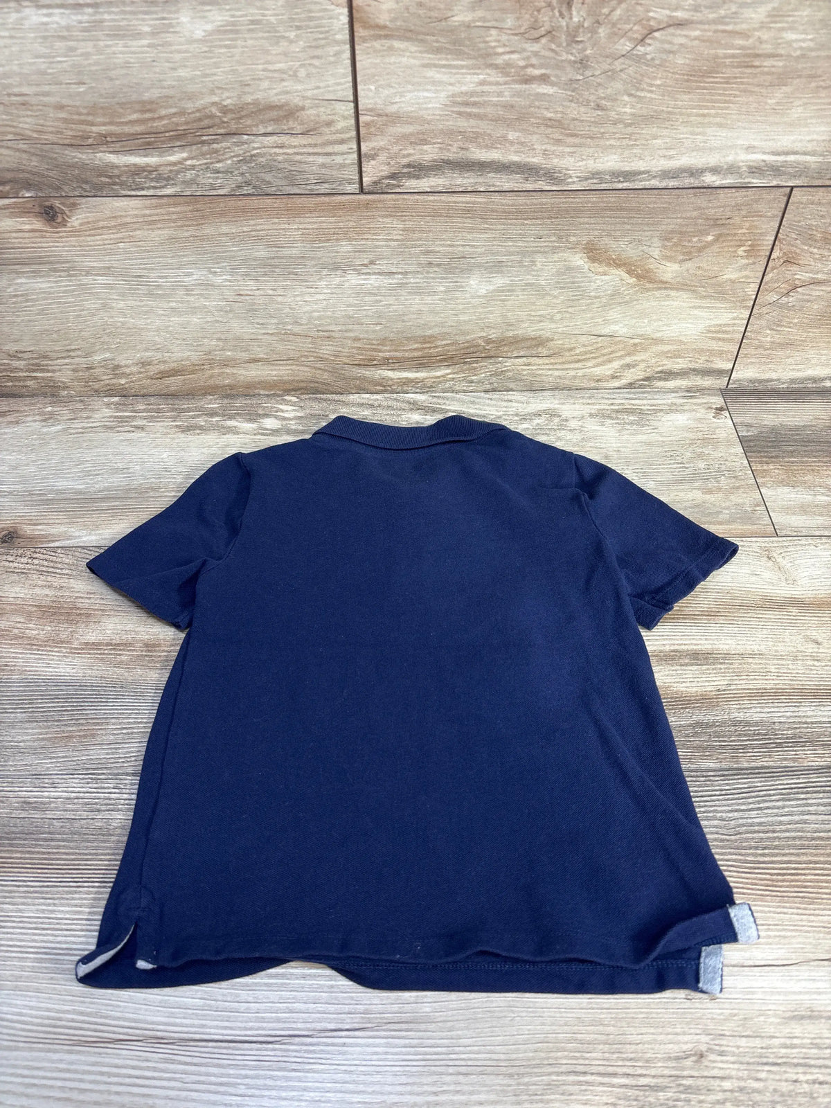 Back view of Old Navy navy polo shirt in size 5T showcasing short sleeves and collar on a wood-look floor