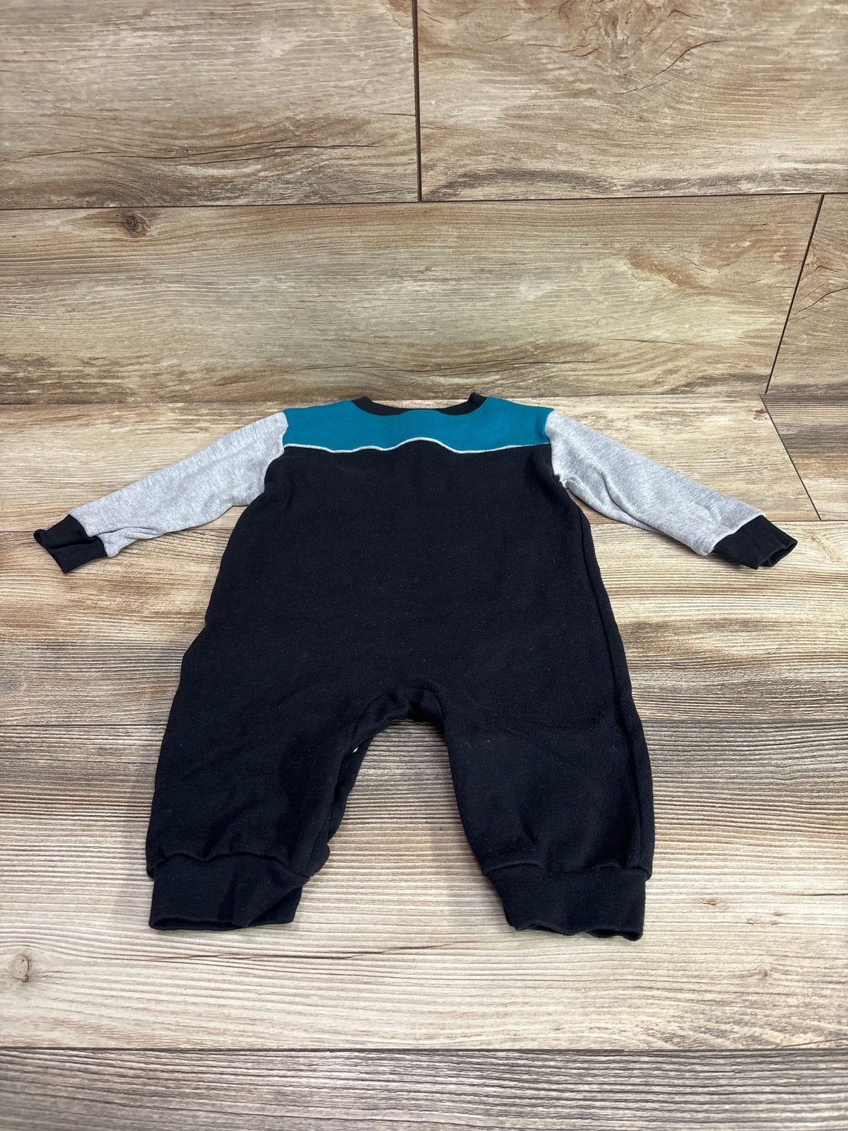 Front view of NFL Team Apparel Jaguars coverall in size 6 to 9 months showcasing gray sleeves and teal yoke on wood flooring