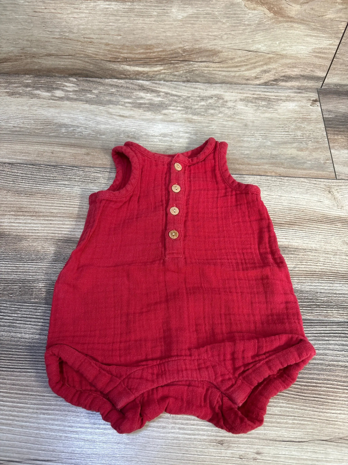 Top-down view of red gauze tank romper 0-3M showing wood buttons and elastic leg openings on wood floor