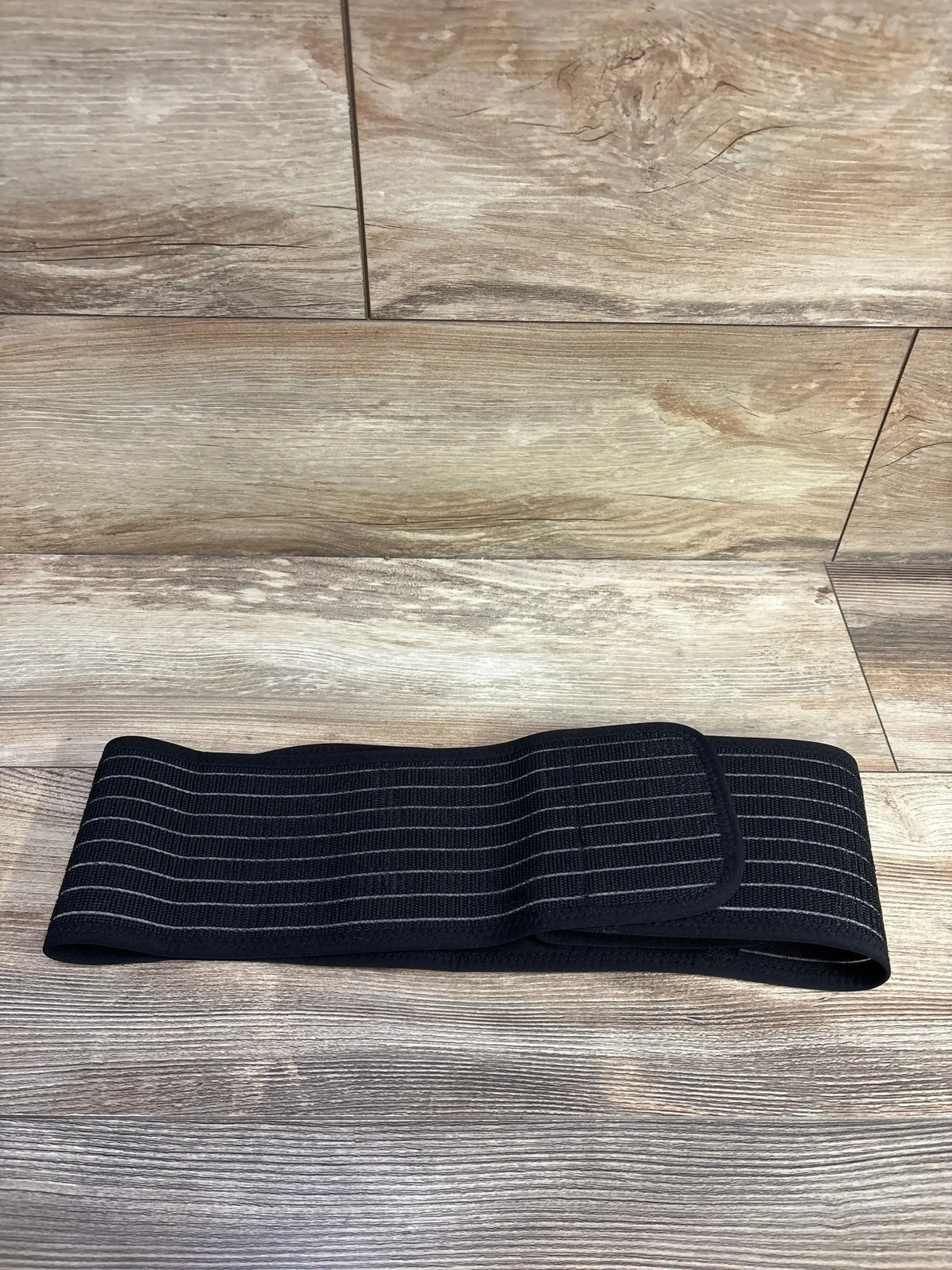 Flat lay of AZMed maternity back support band showing elastic ribbing and Velcro closure on woodgrain background