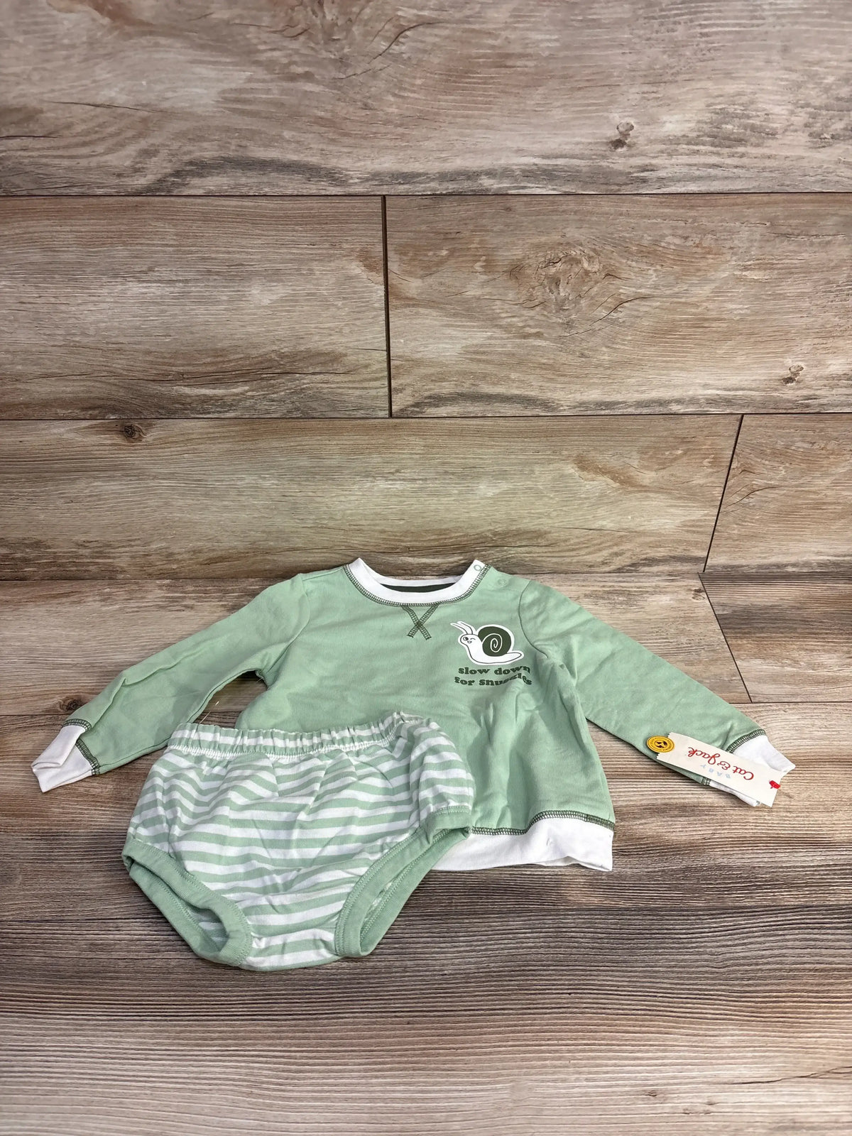 Green baby outfit set with long sleeve snail top and striped shorts on wood background