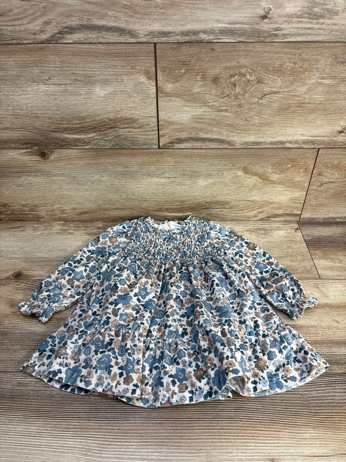 Flat lay of Mayoral ruffled velvet dress sz 12m showcasing ivory fabric with blue and tan floral print smocked bodice and long sleeves on wood floor