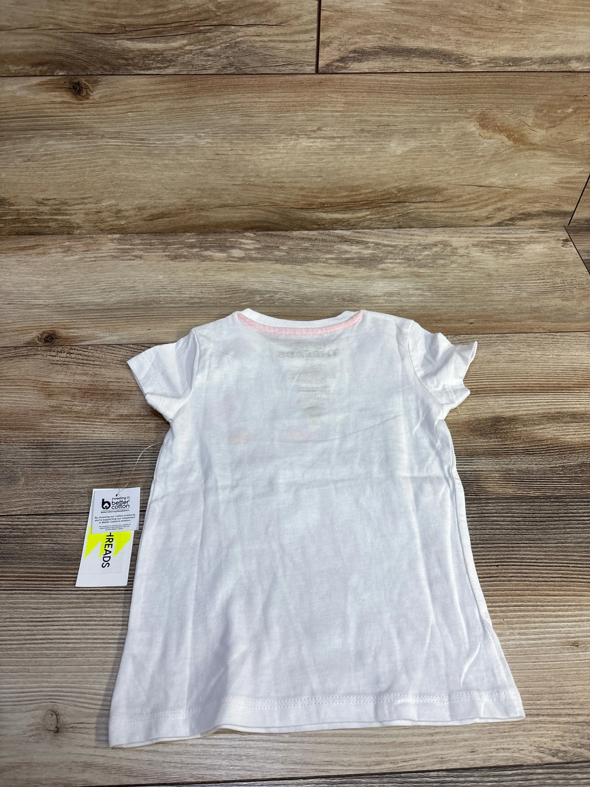 Back view of white Epic Threads Hello Kitty T-shirt (2T) with pink neckline, short sleeves, attached tag on wood background