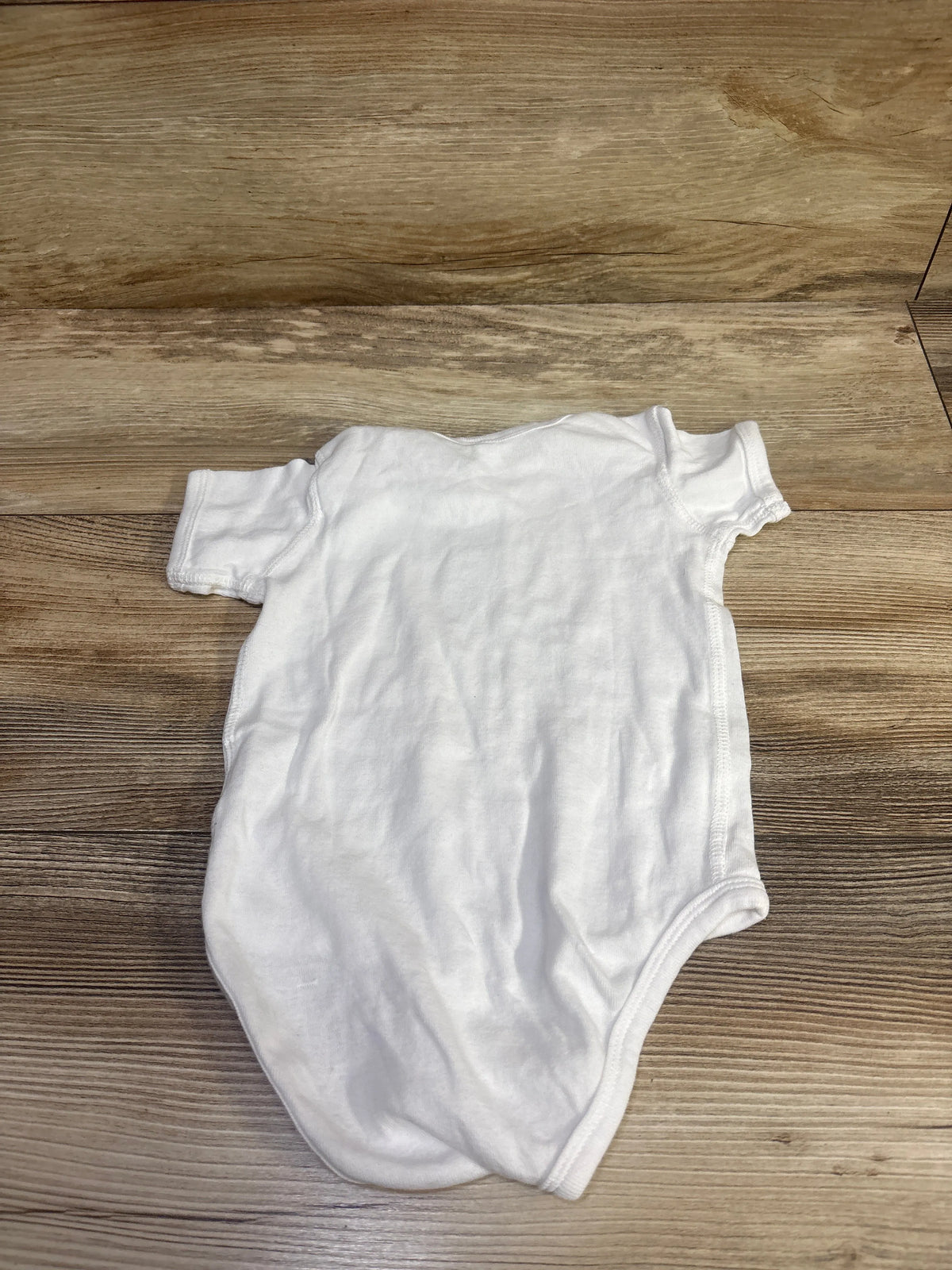 Back view of white Rabbit Skins The Office Dwight bodysuit in size 18 months showing a blank back on a wood floor