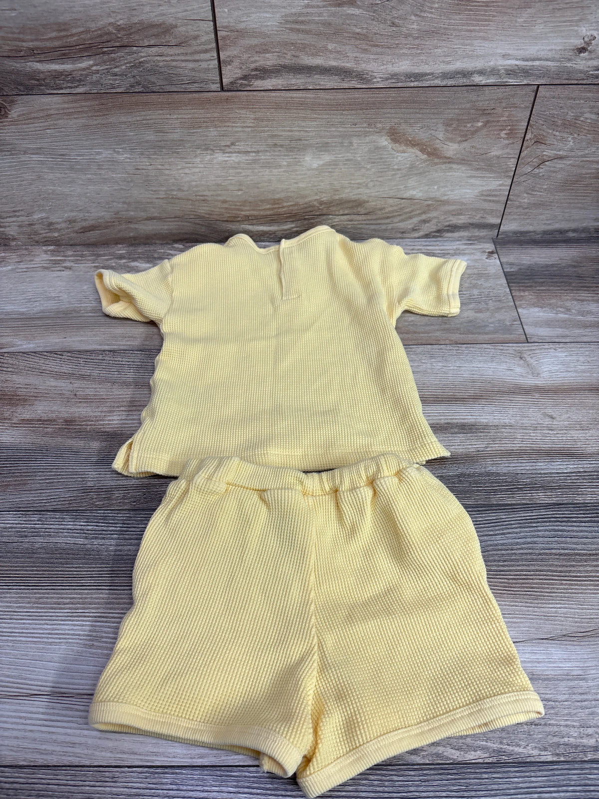 Top-down view of H&M 2-piece yellow waffle knit shirt and shorts set showcasing textured knit fabric on a wood floor