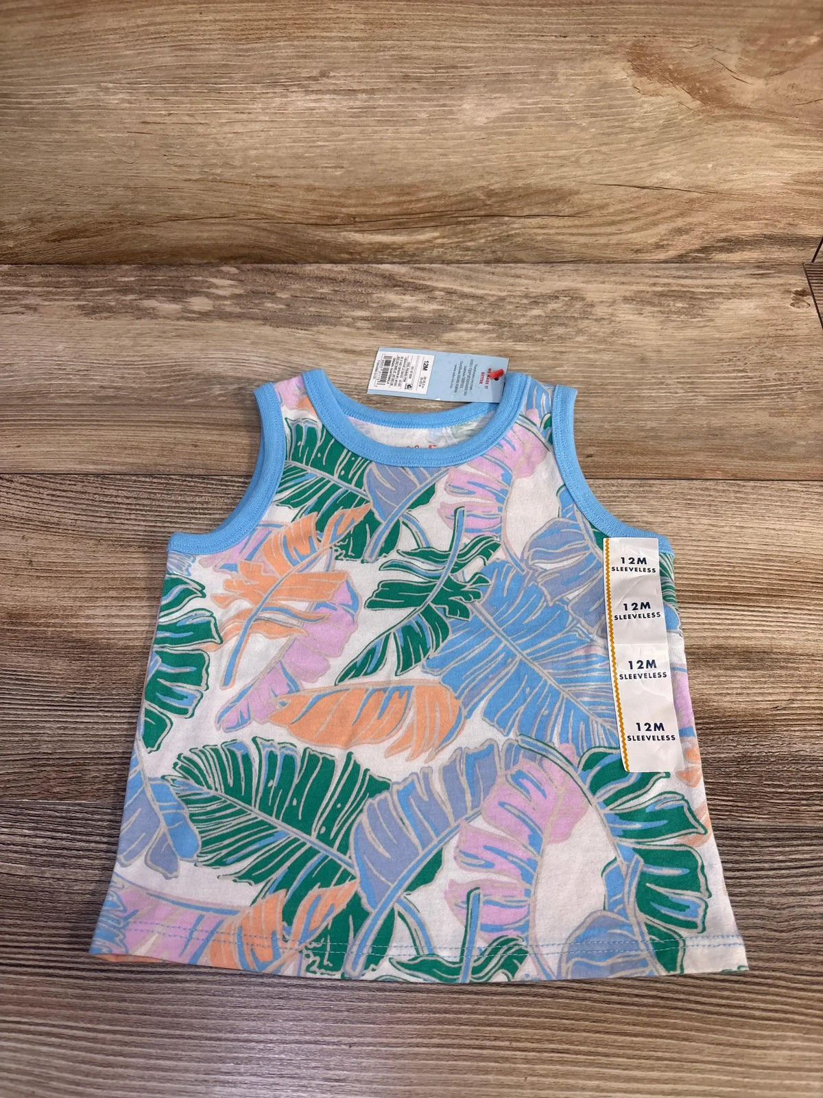 Front view of NEW Cat and Jack tropical leaf print tank top size 12m with blue trim and hangtags on wood plank flooring