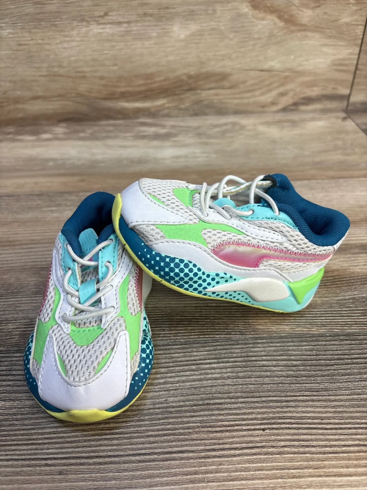 Front three-quarter view of Puma RS-X3 WR toddler sneakers, white with multicolor accents, mesh upper on wooden floor