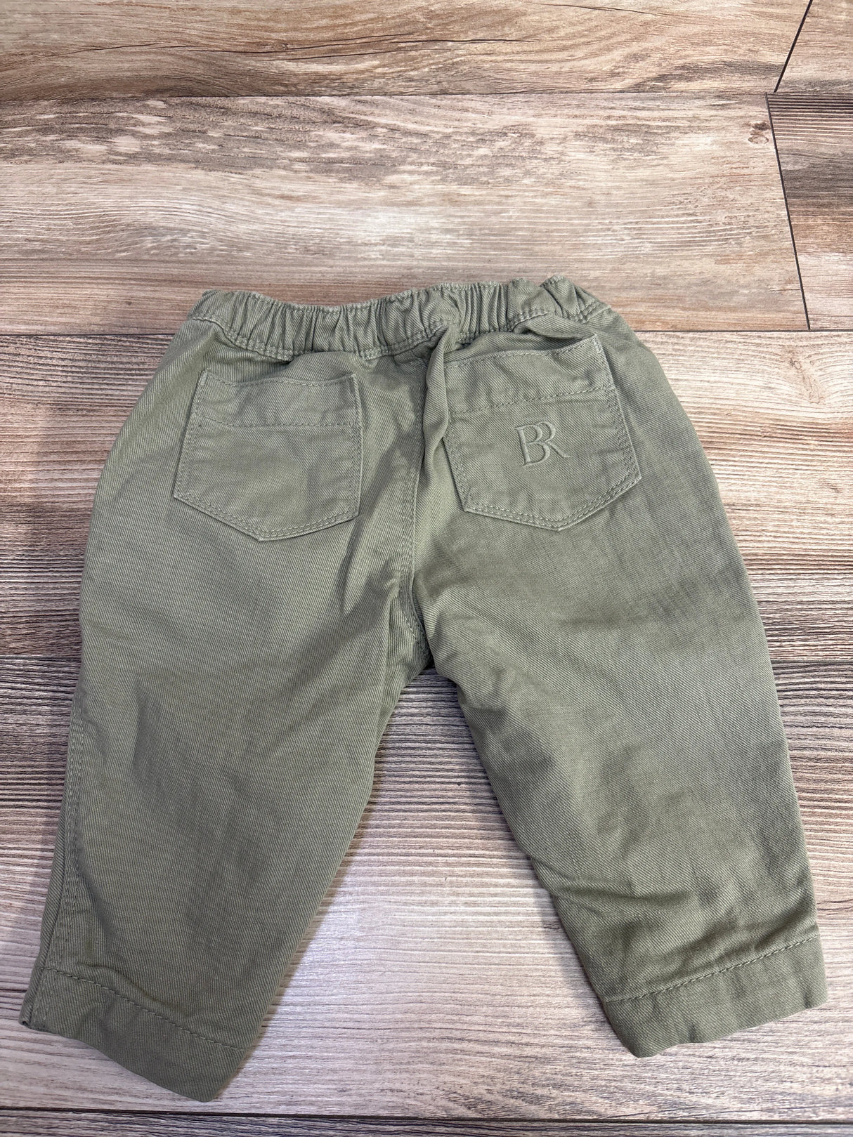 Back view of toddler olive green pants with elastic waistband and two pockets on wooden floor