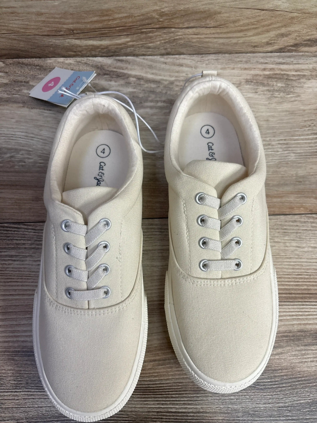 Top view of Cat & Jack slip-on canvas sneakers in off-white showing elastic laces, white rubber soles on wood floor
