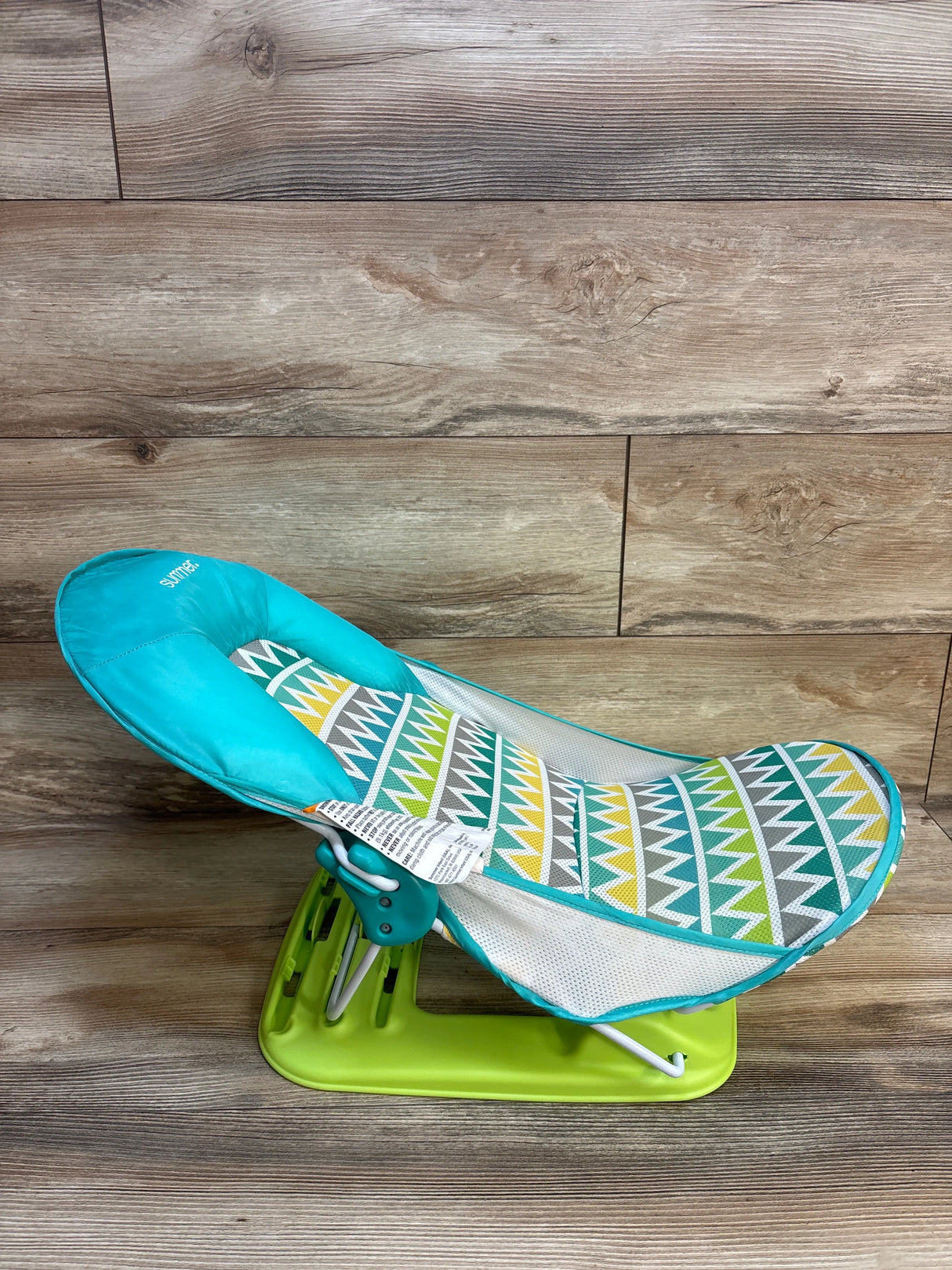 Colorful baby bouncer seat with geometric pattern and green base on wood floor