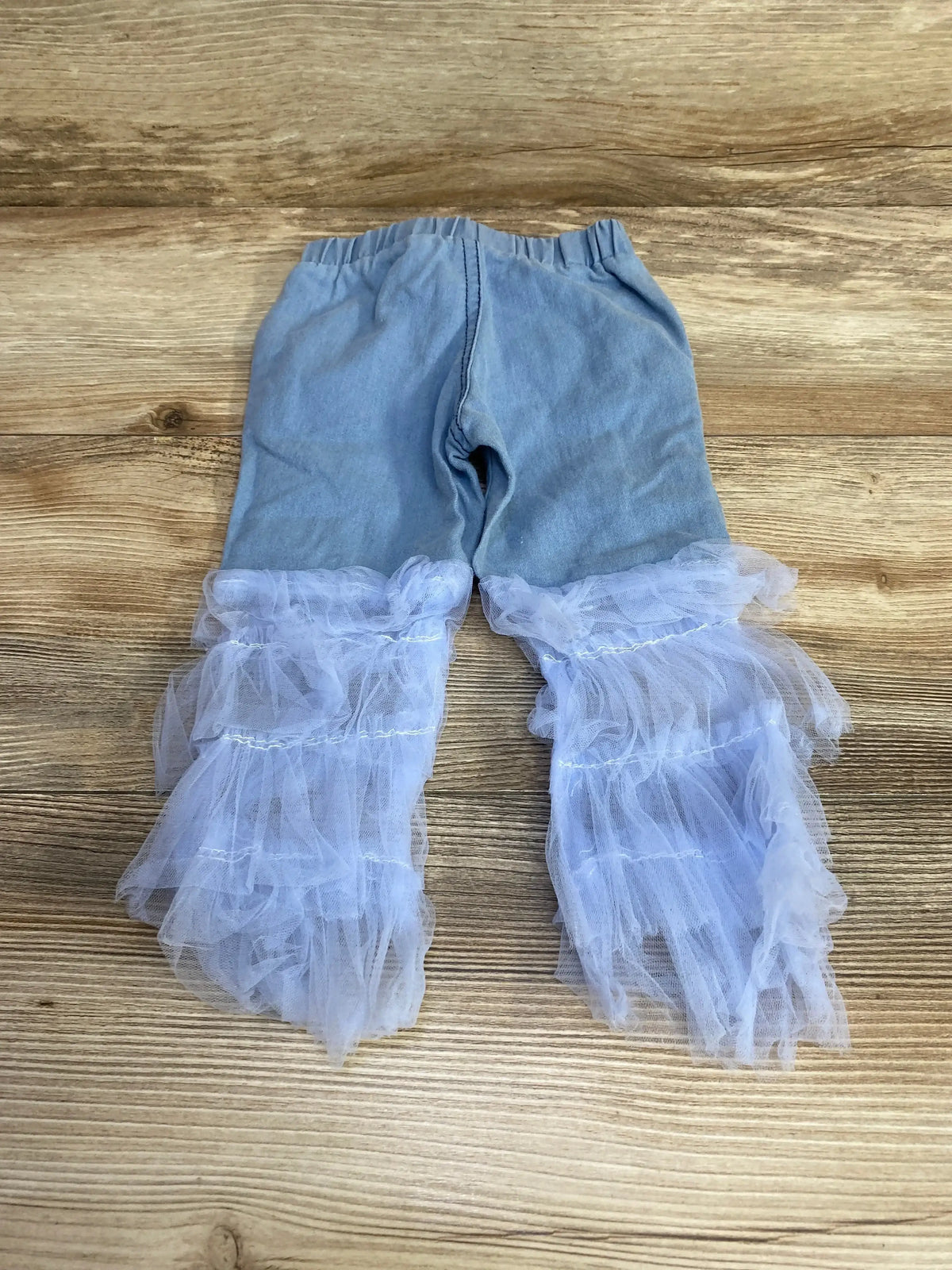 Flat lay of blue distressed baby jeans size 12 months showing layered white tulle ruffle tiers on the lower legs on wood background