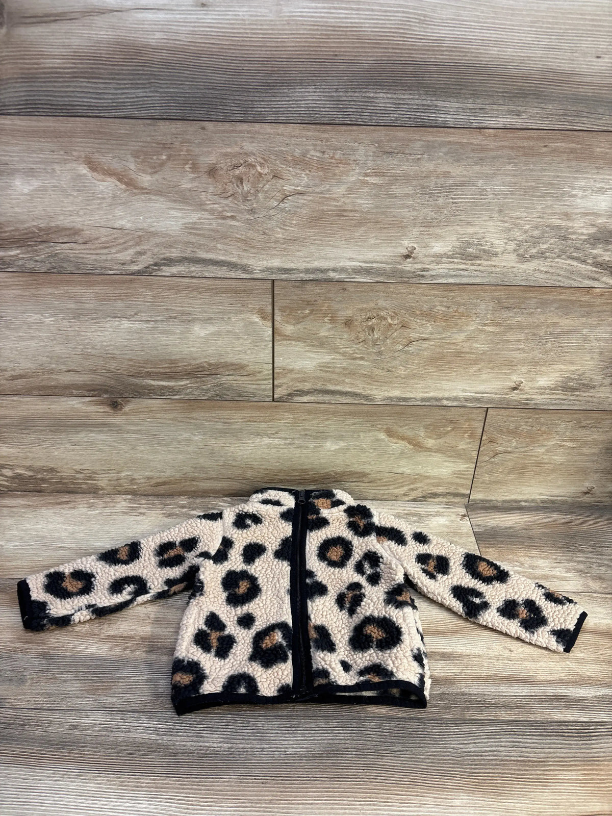 Flat lay of Children’s Place toddler sherpa jacket in tan leopard print showing front zipper, long sleeves, and black trim on wood background