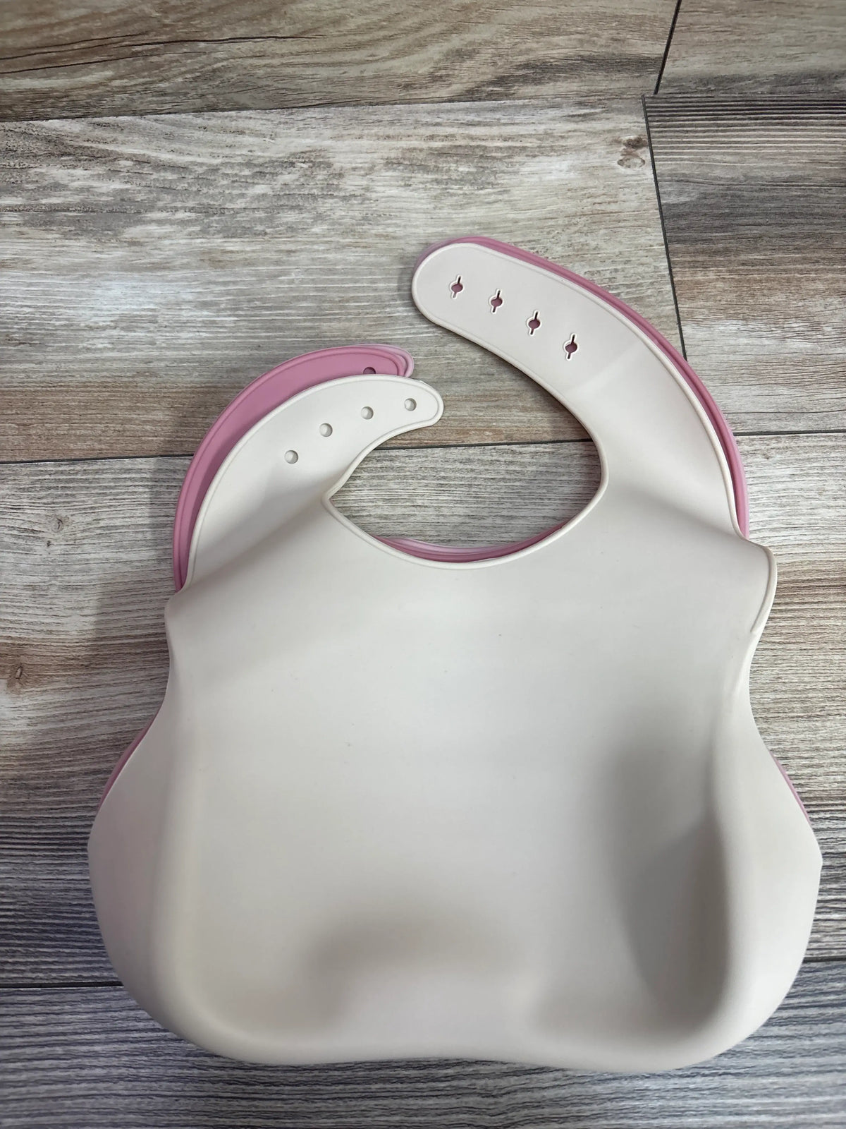 Two PandaEar silicone baby bibs with catch pockets in cream and pink on a wooden surface.