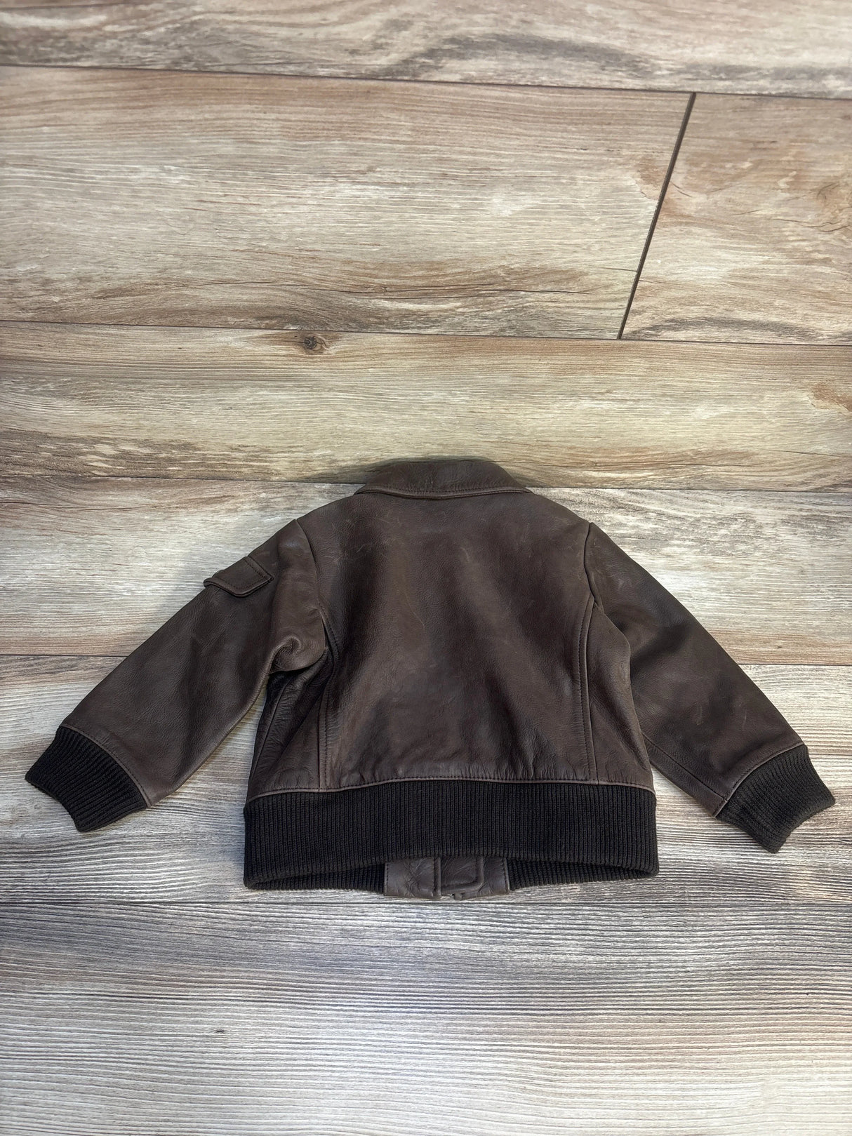 Back view of Banana Republic Heritage leather flight jacket, toddler 12-24 months, showing black ribbed cuffs and hem on wood floor