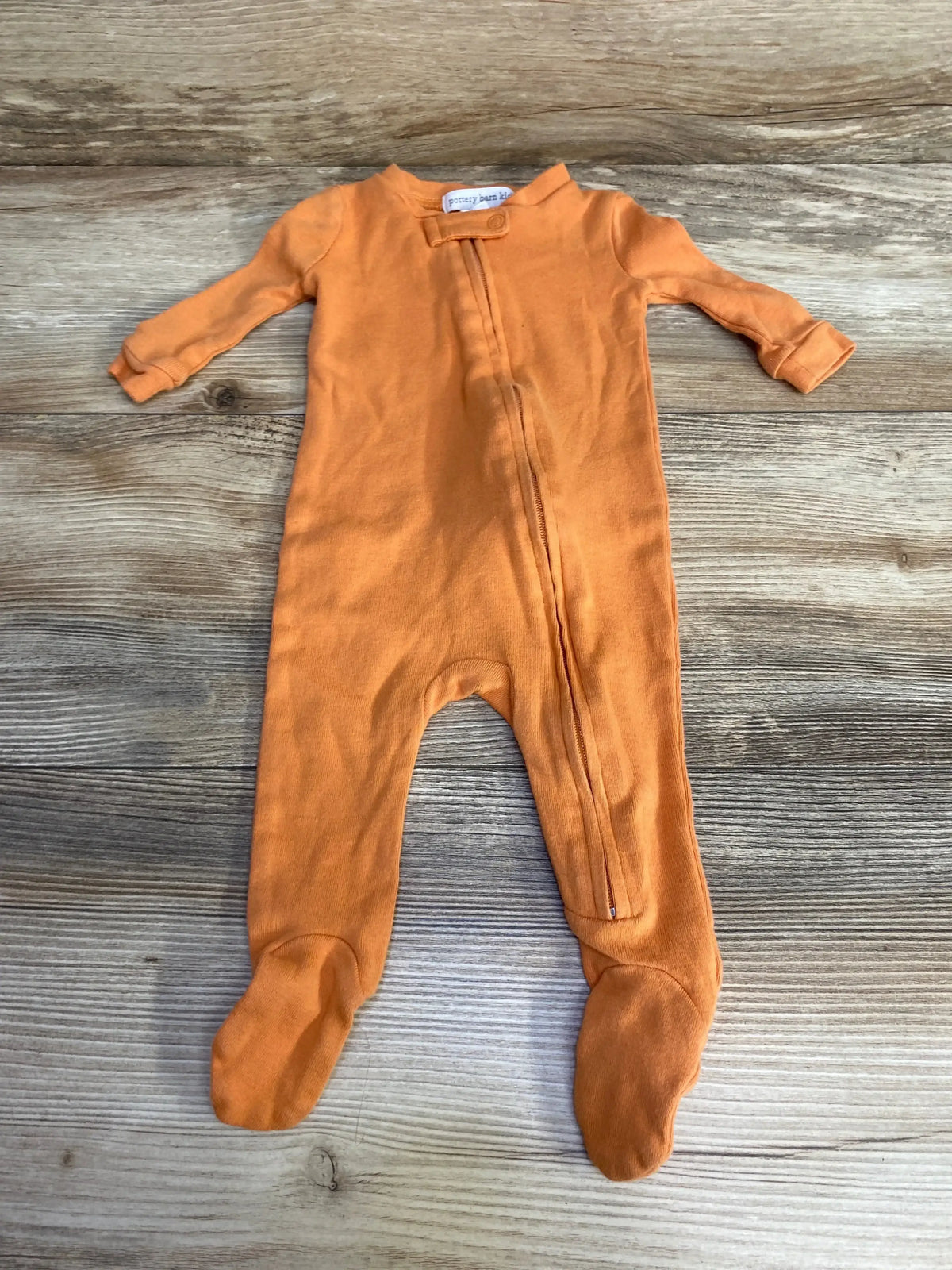 Front view of Pottery Barn Kids orange footed sleeper size 0-3M showcasing center zipper and snap closure at neckline on wood background
