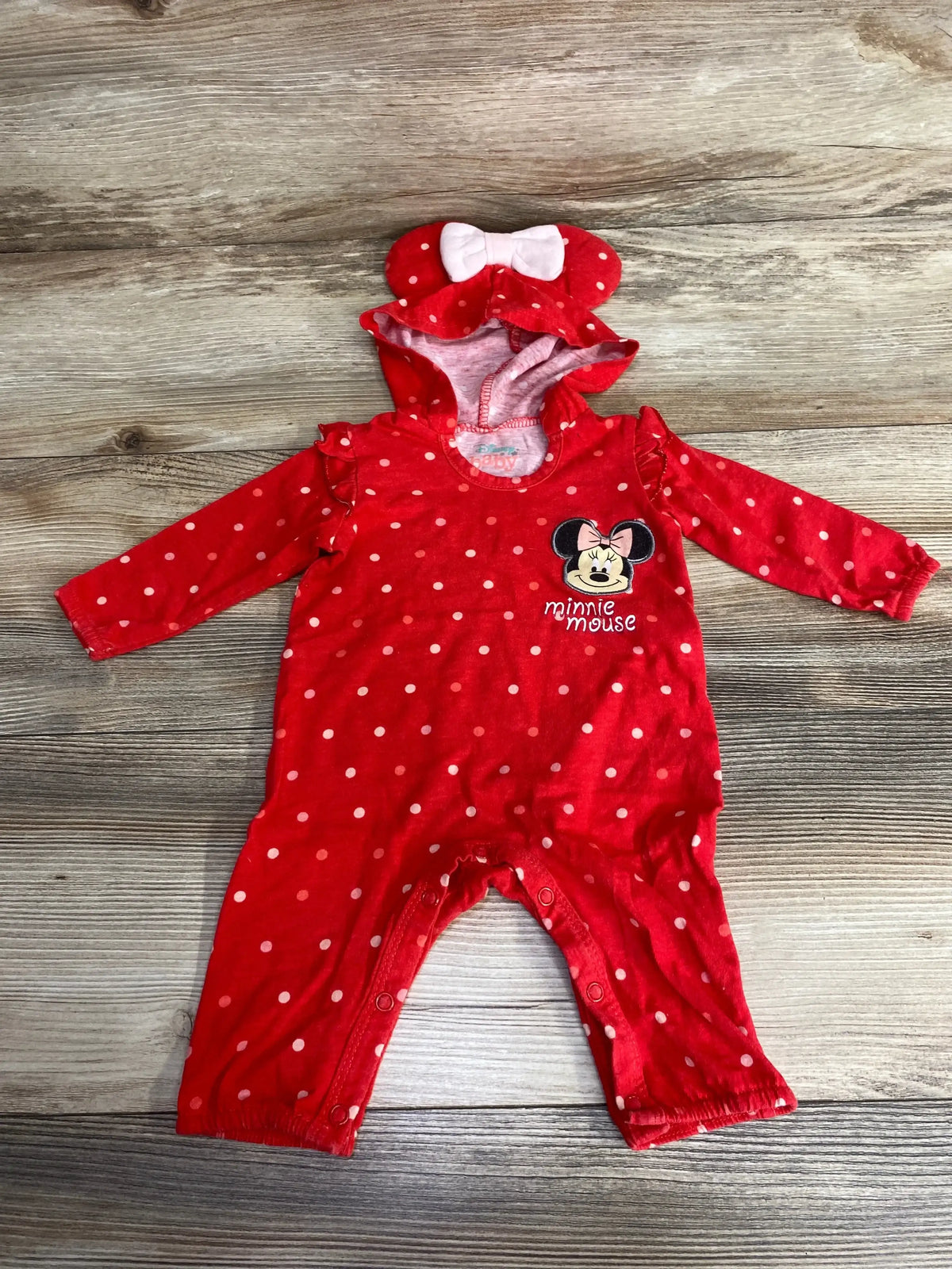 Red polka dot baby romper with Minnie Mouse design and bow hood on wood background