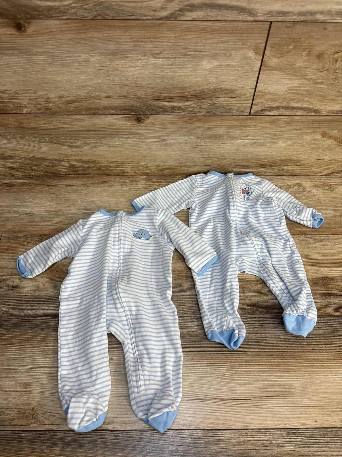 Blue and white striped baby footed pajamas with elephant and dog appliques, laid on wood floor