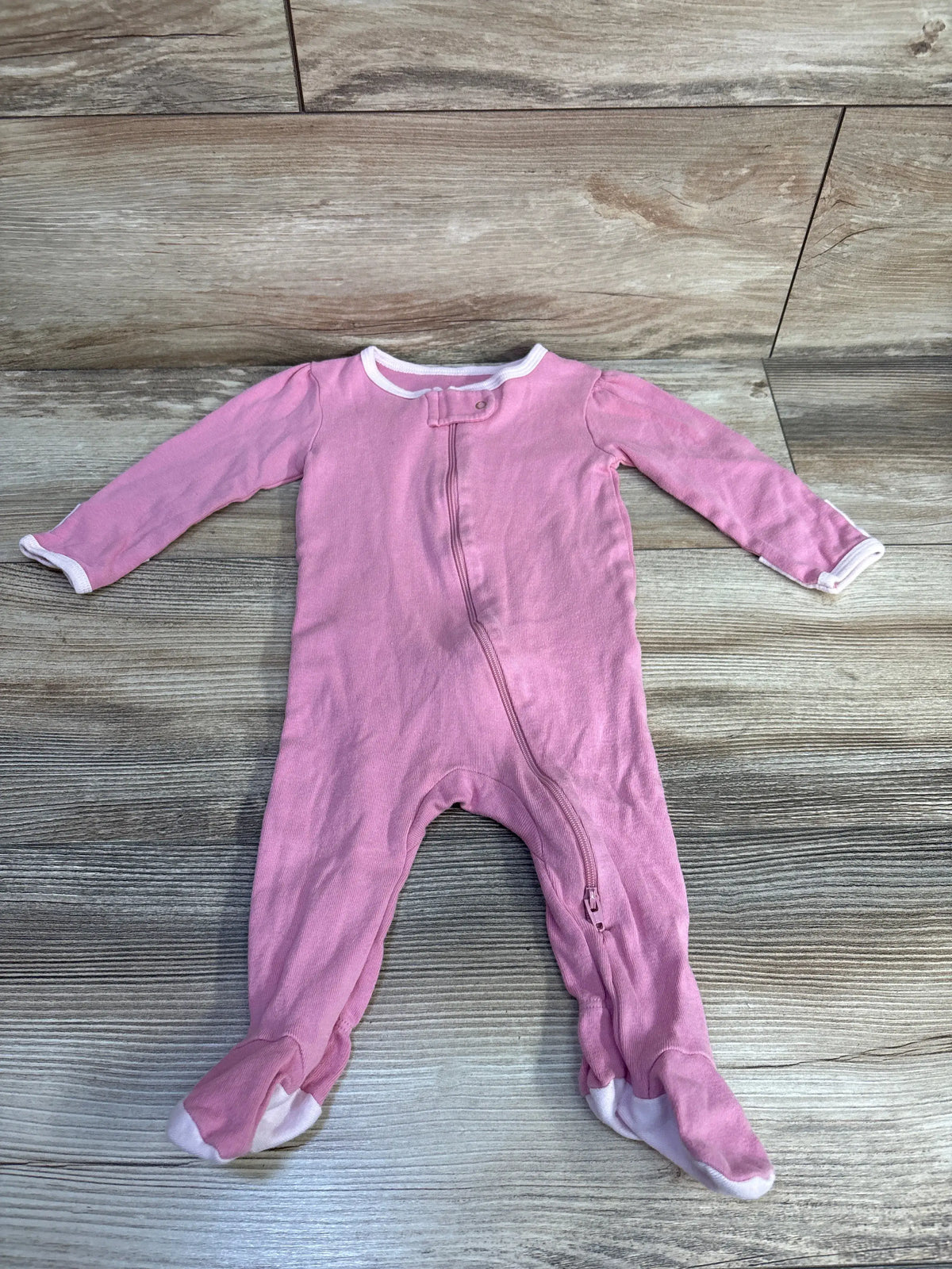 Front view of Cloud Island pink baby sleeper showcasing long sleeves, footed legs, and front zipper on a wood surface