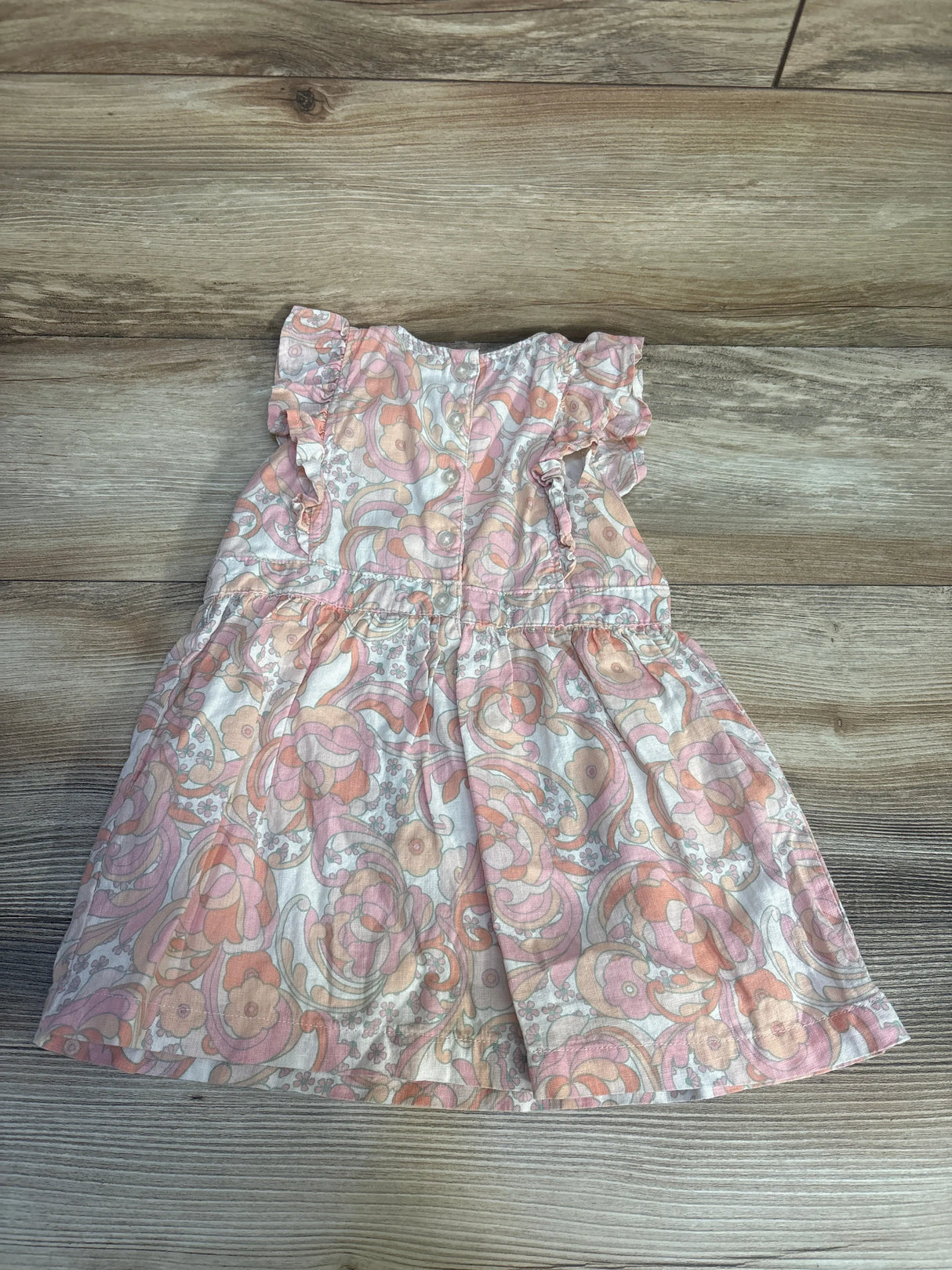Floral ruffle sleeve toddler dress with pink and orange swirl pattern on wood background