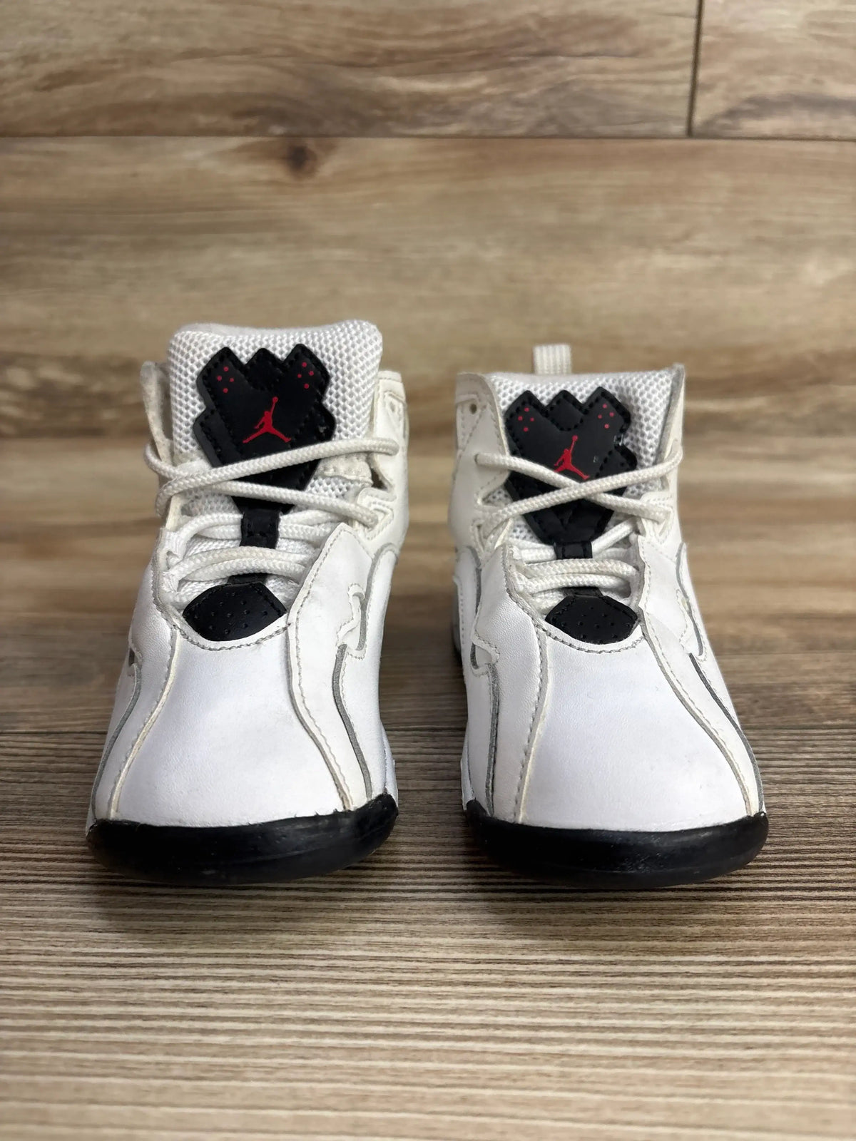 Pair of white toddler Air Jordan basketball shoes with black and red logos on wooden floor