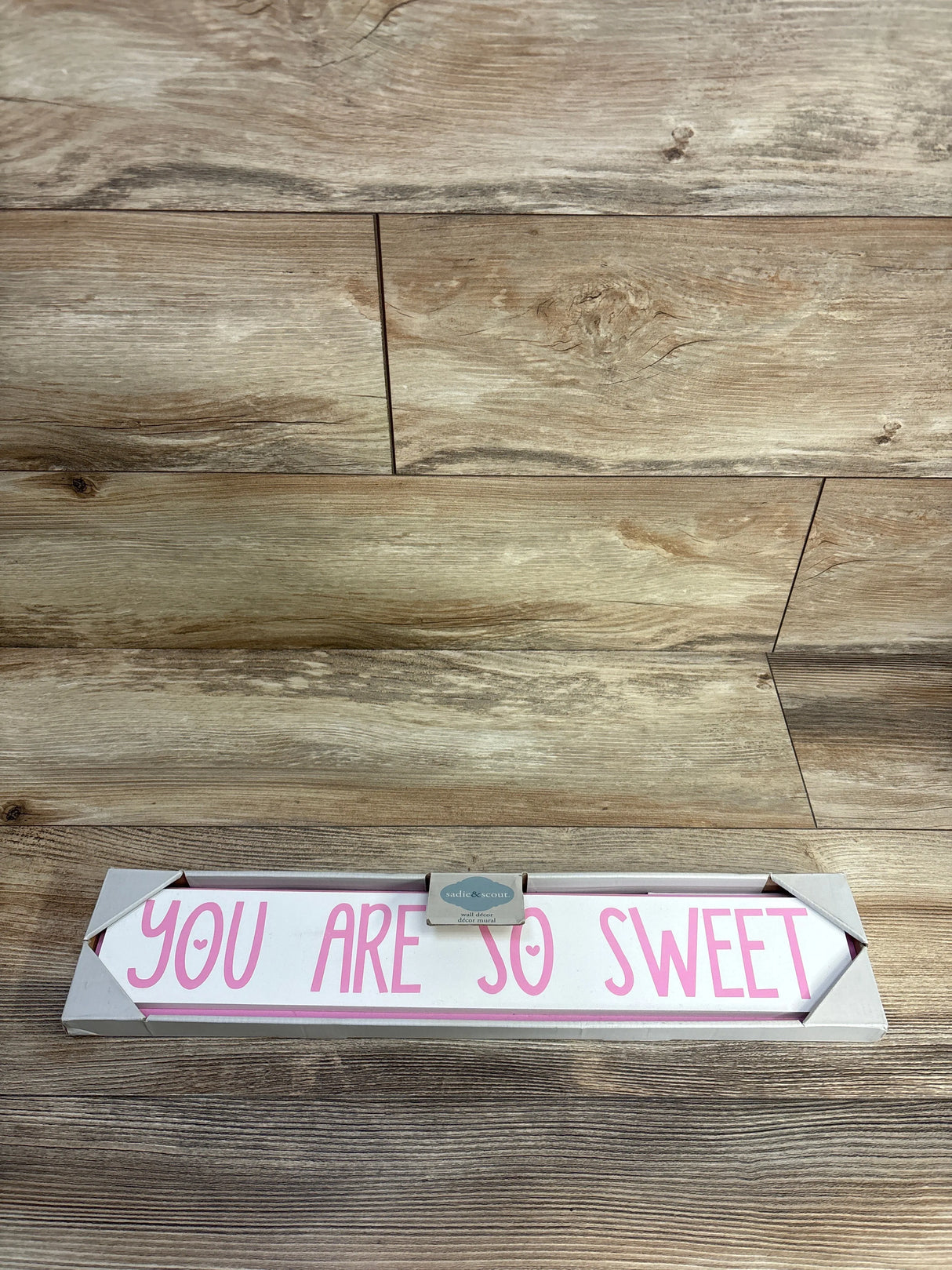 Wooden sign with pink lettering reading 'You Are So Sweet' on wood surface, nursery decor.