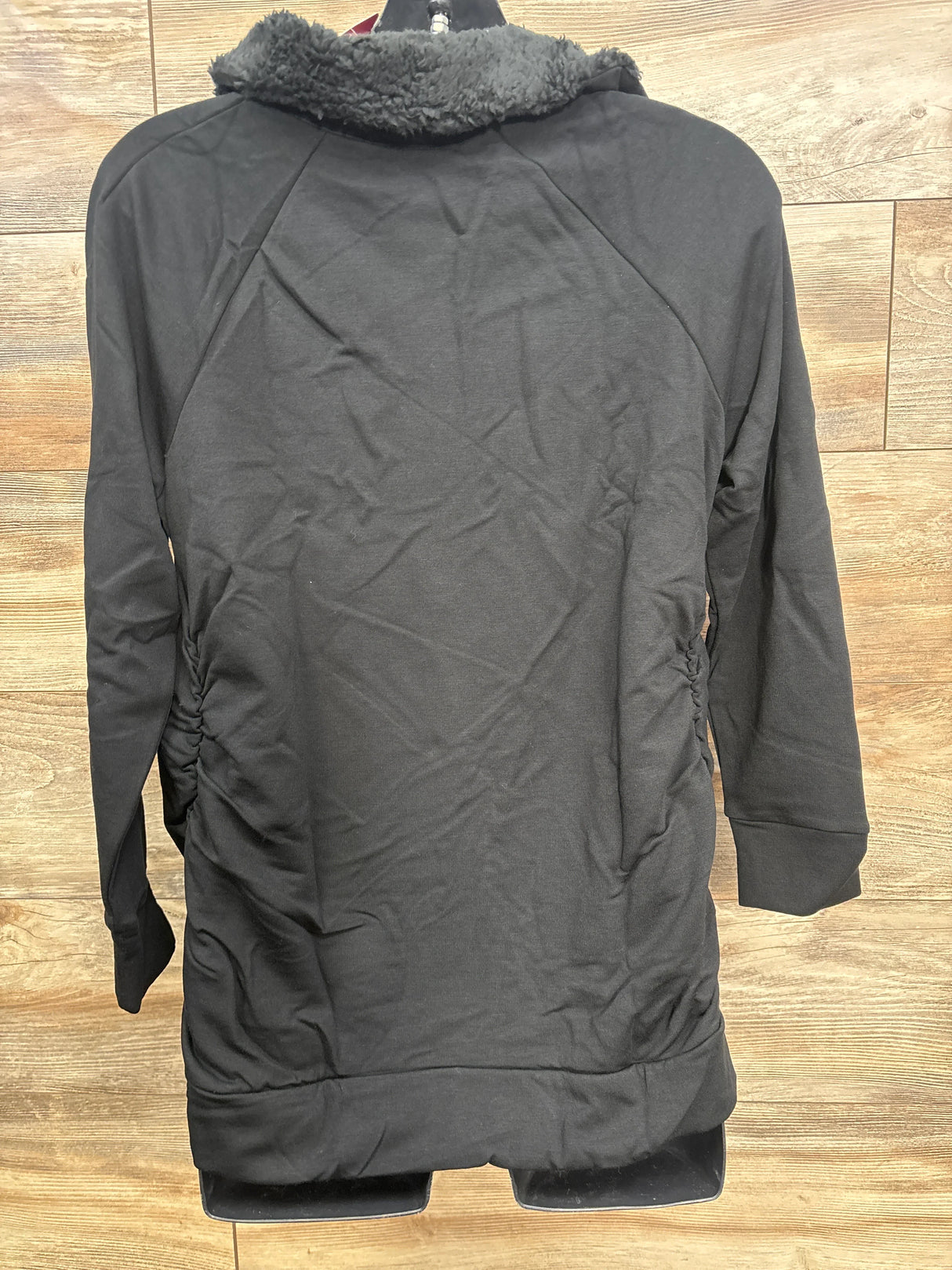 Black long-sleeve sweatshirt with ruched sides and fuzzy collar detail on wooden floor