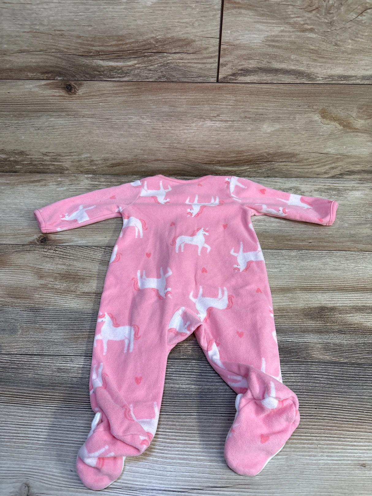 Flat lay of Child Of Mine pink blanket sleeper 0-3M with white unicorn print and built-in feet on wood background