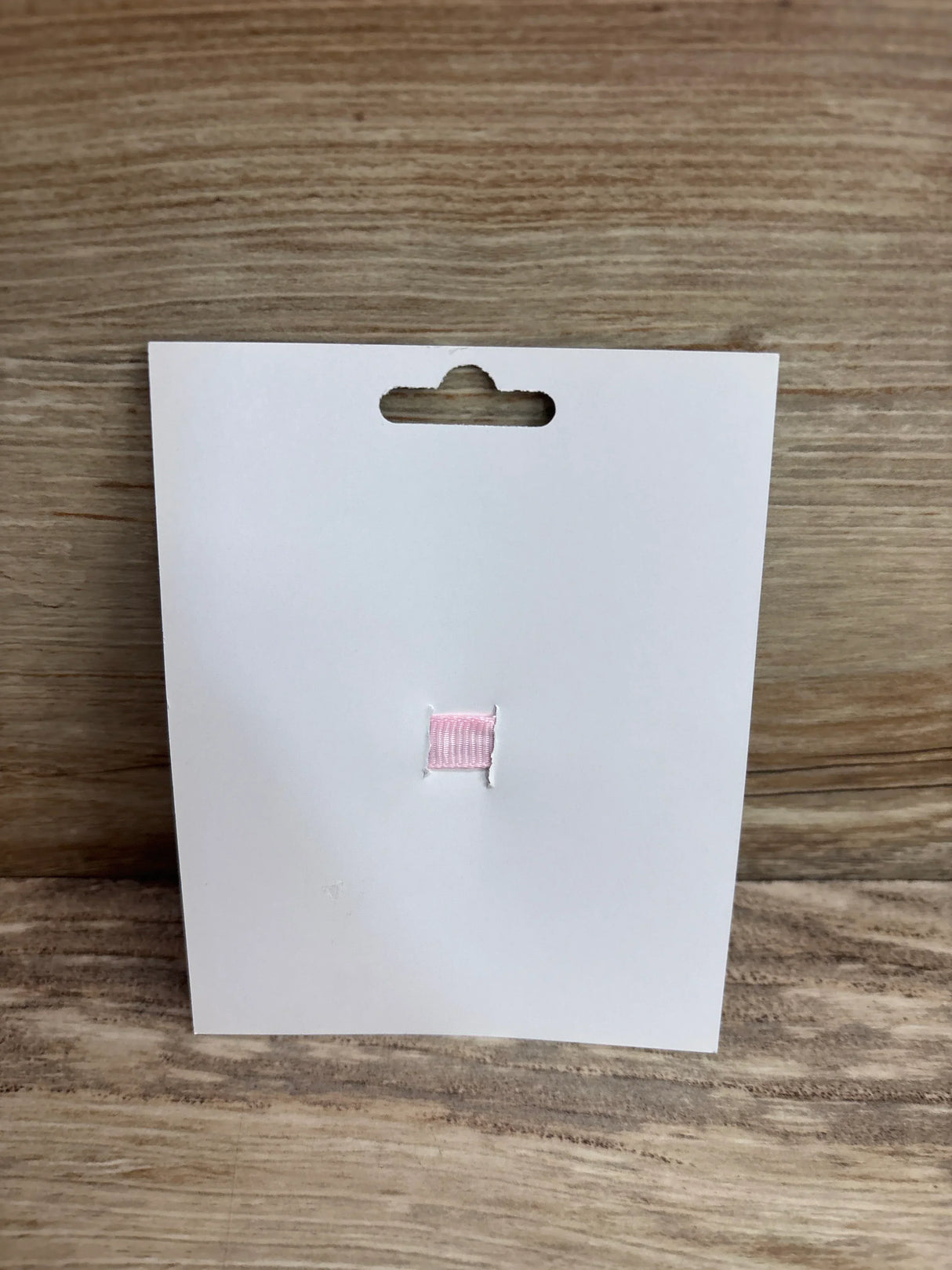 Front view of lollipop applique hair bow on white display card showing small pink ribbon applique against wood background