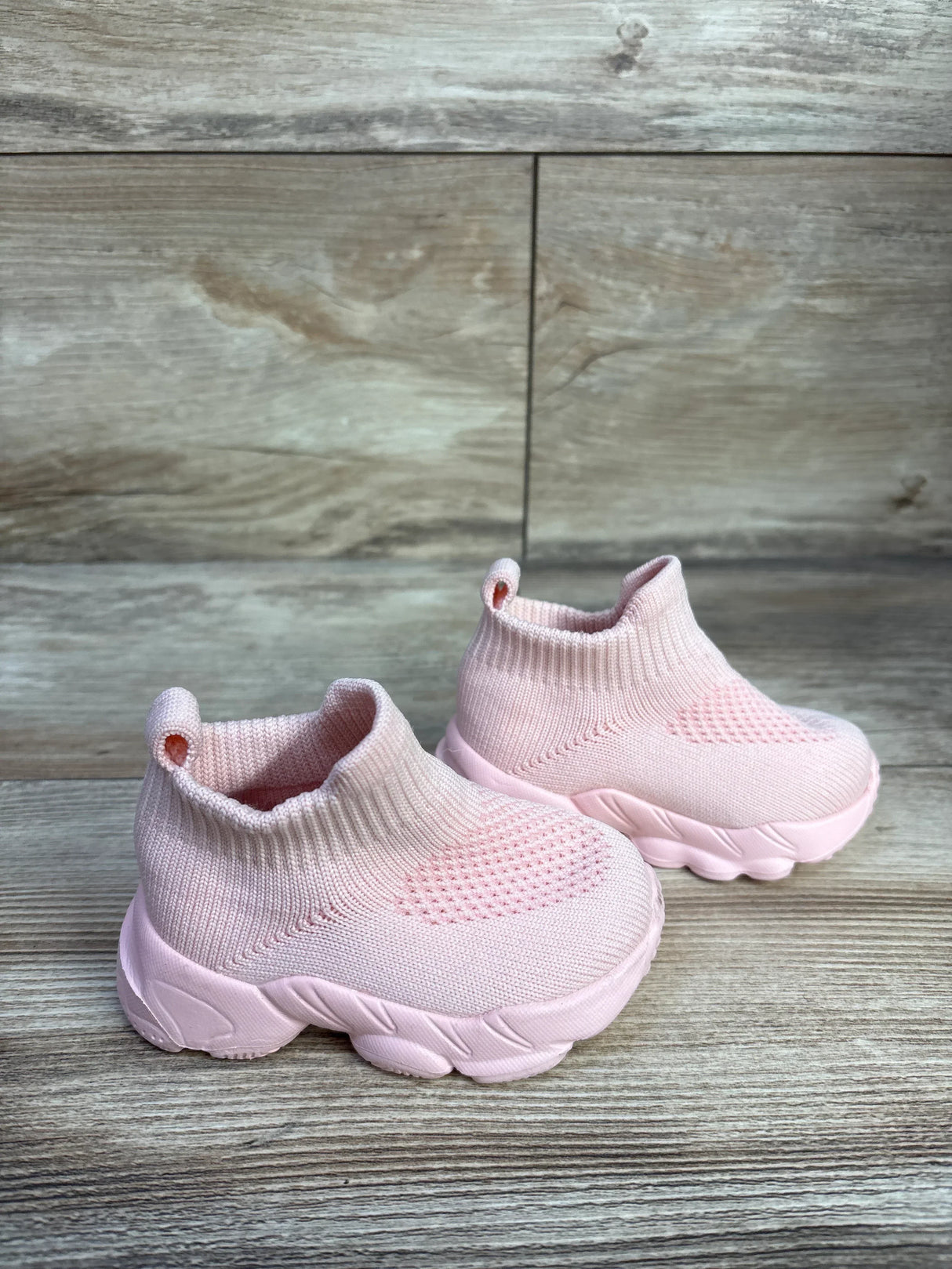 Three-quarter view of pink baby high-top sock shoes showcasing knit upper and chunky sole on wood background