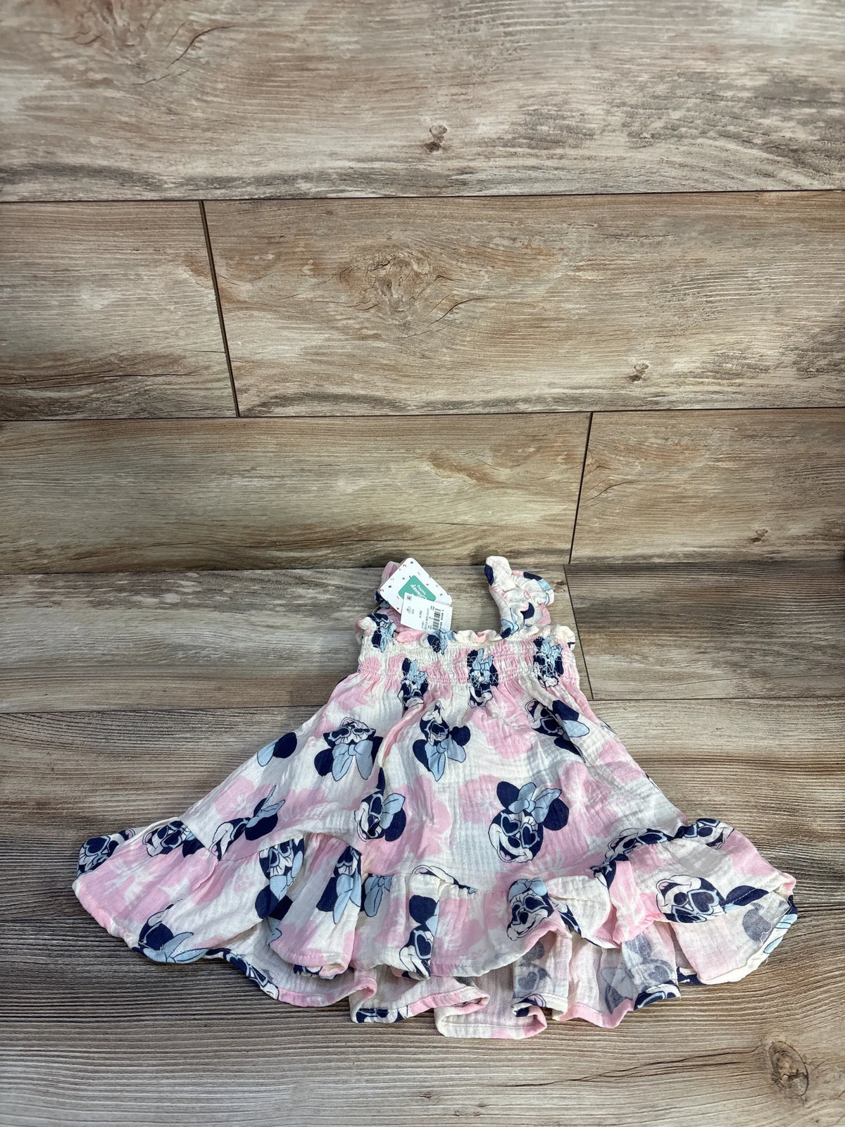 Front view of pink Disney Baby Minnie Mouse smocked gauze dress and bloomers set on wood floor