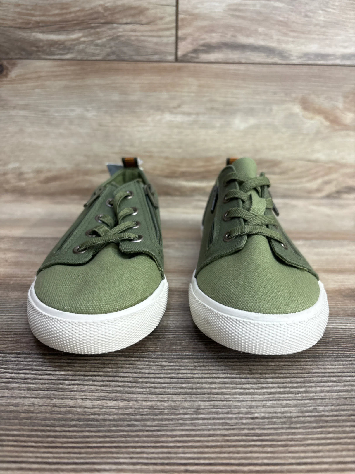 Pair of green kids canvas sneakers with white rubber soles on wooden floor