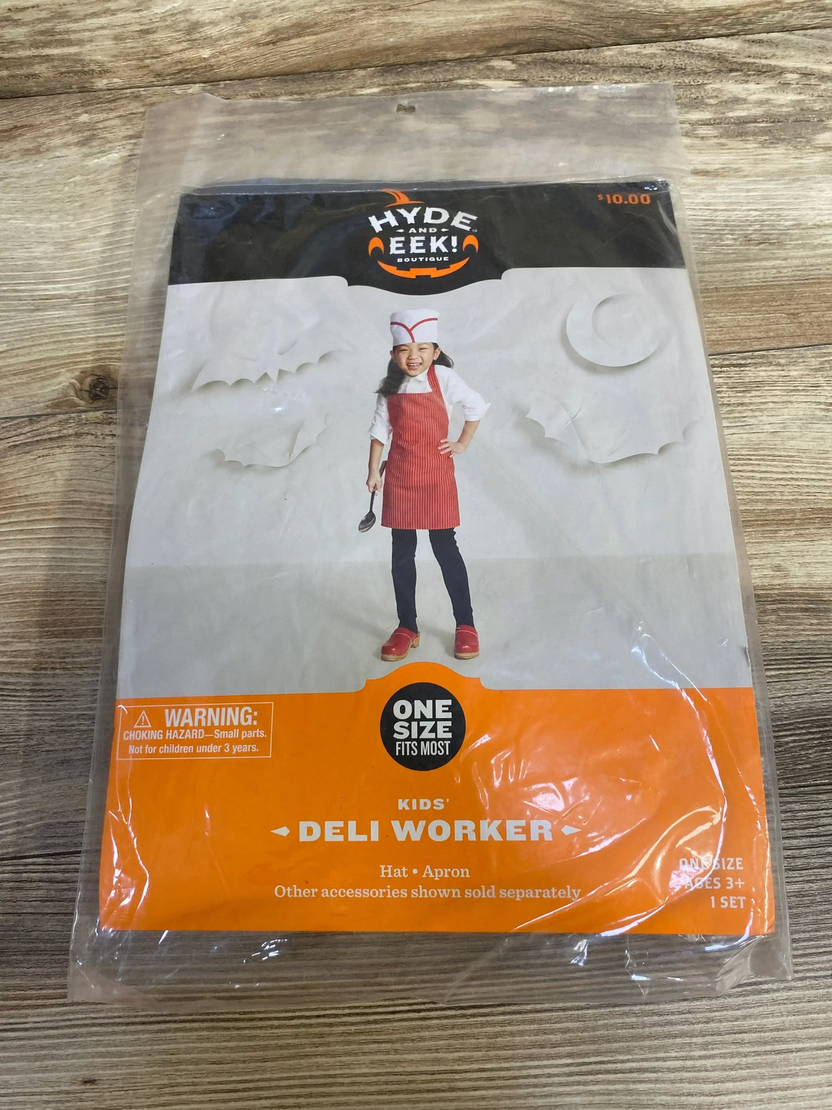 Front view of Hyde and Eek! Deli Worker costume showing a red apron and matching hat in sealed packaging on a wood surface
