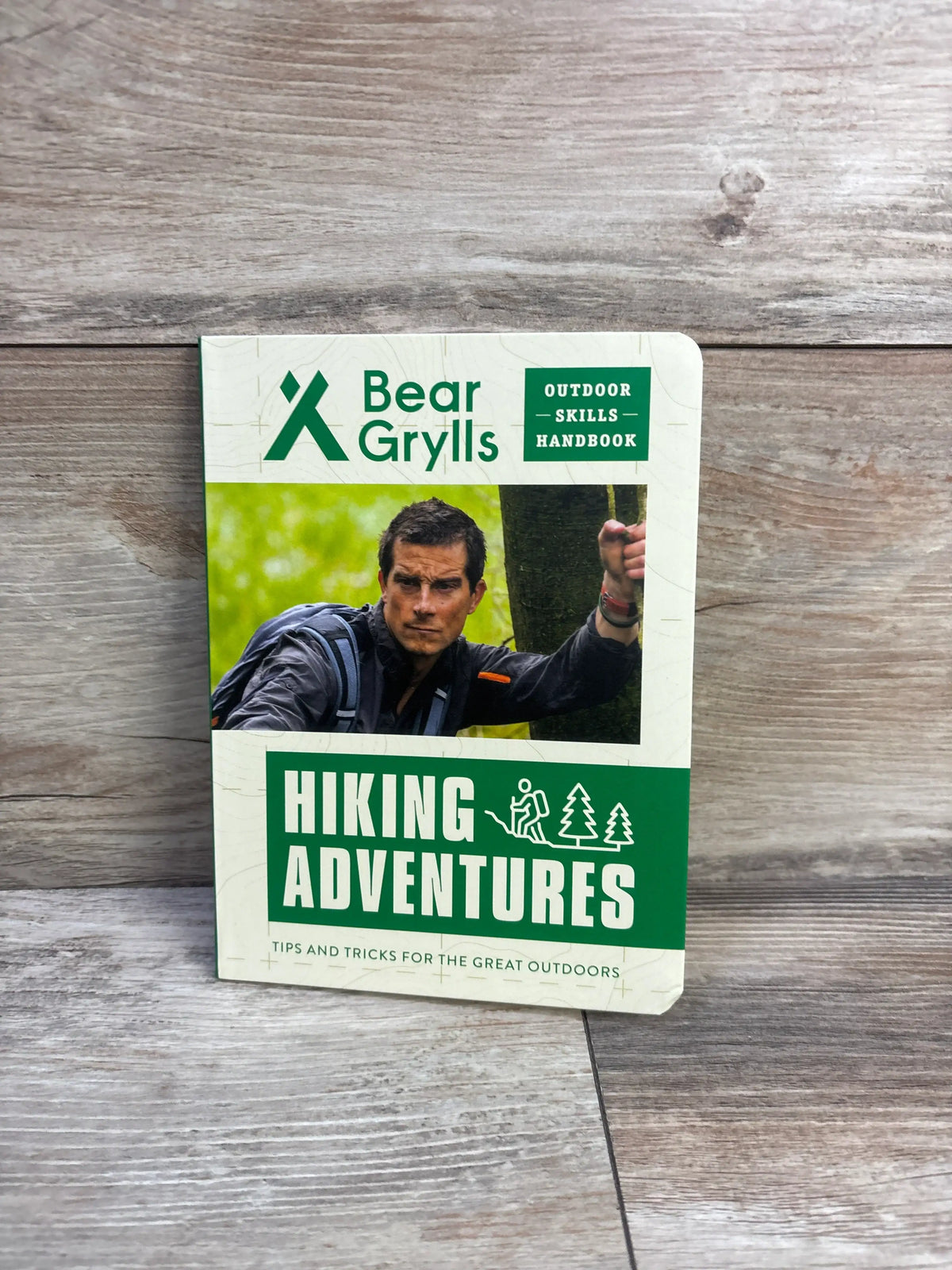 Front view of Hiking Adventures Bear Grylls Outdoor Skills Handbook Paperback showing Bear Grylls on a wood grain surface