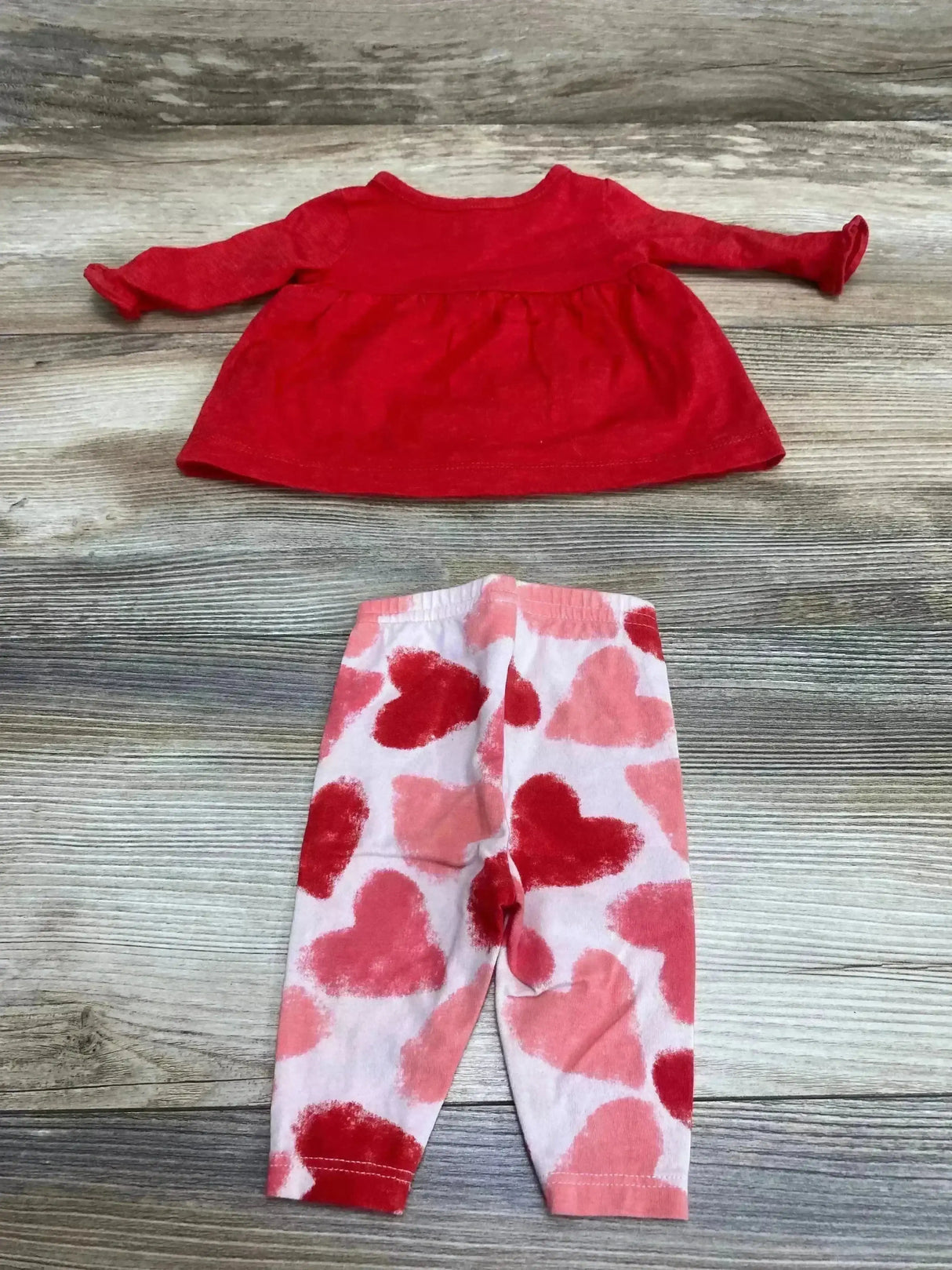 Flat lay of newborn two-piece: red Henley top and white leggings with pink and red hearts on wood