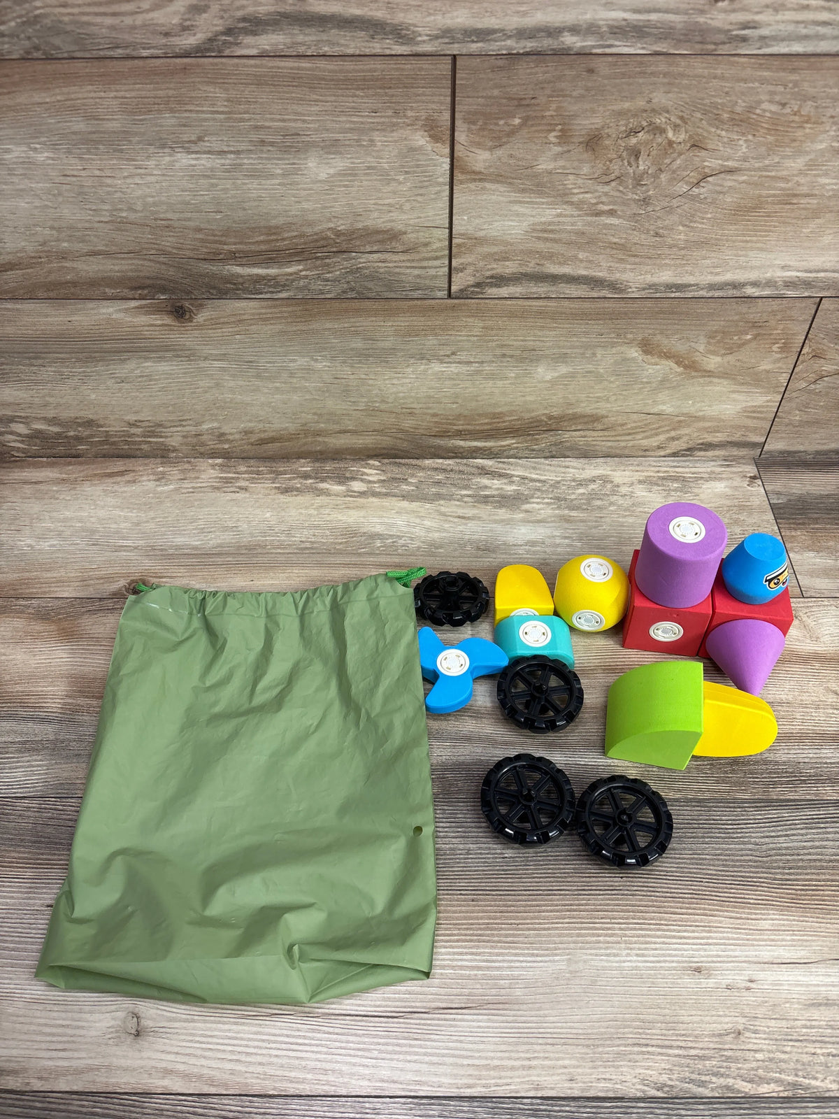 Top view of Hodurgyi 15pc Magnetic Foam Blocks with Wheels showcasing colorful shapes, black wheels, and green bag on wood floor