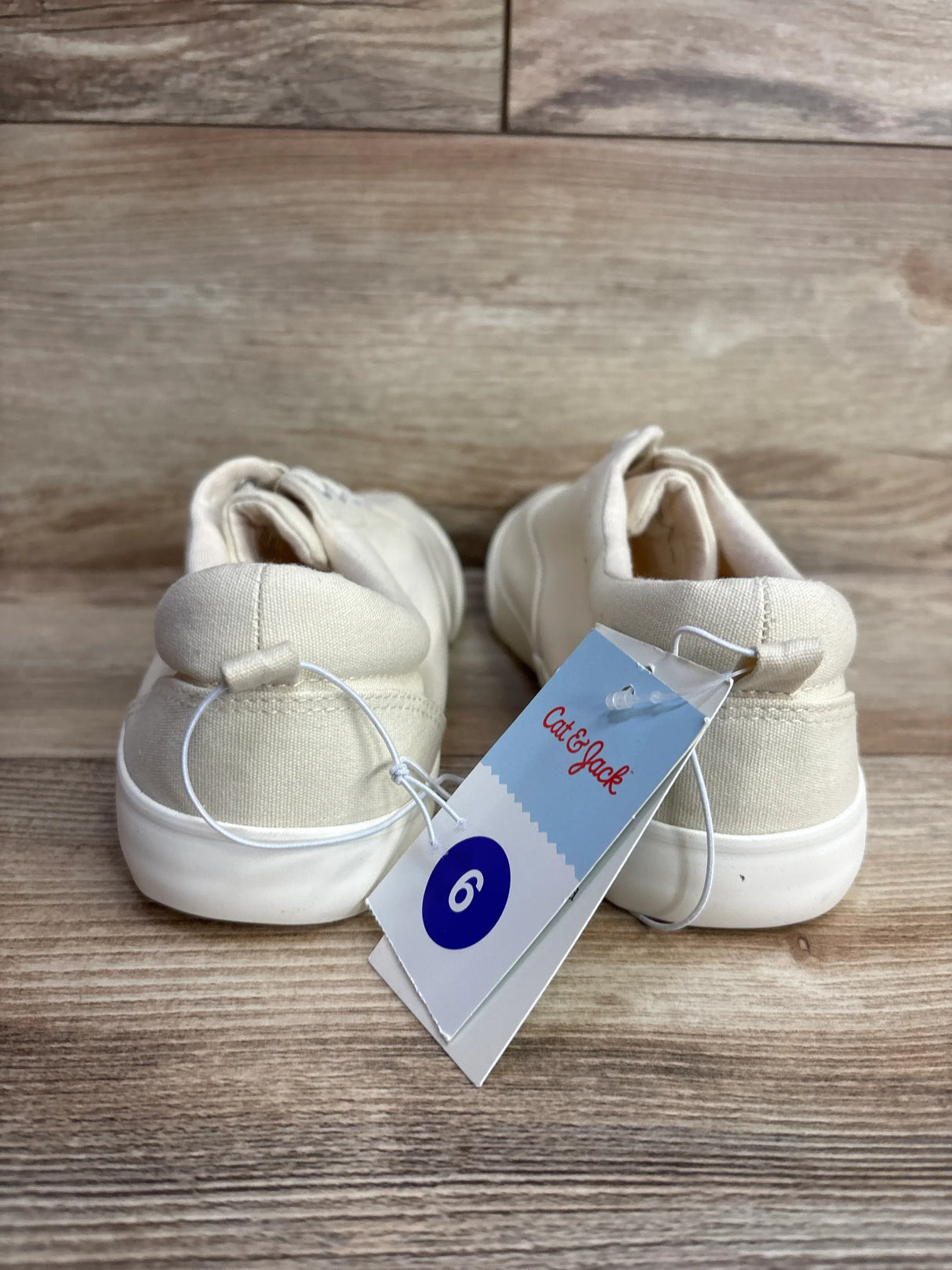 Beige toddler sneakers with white soles and size 6 Cat & Jack tag on wooden floor