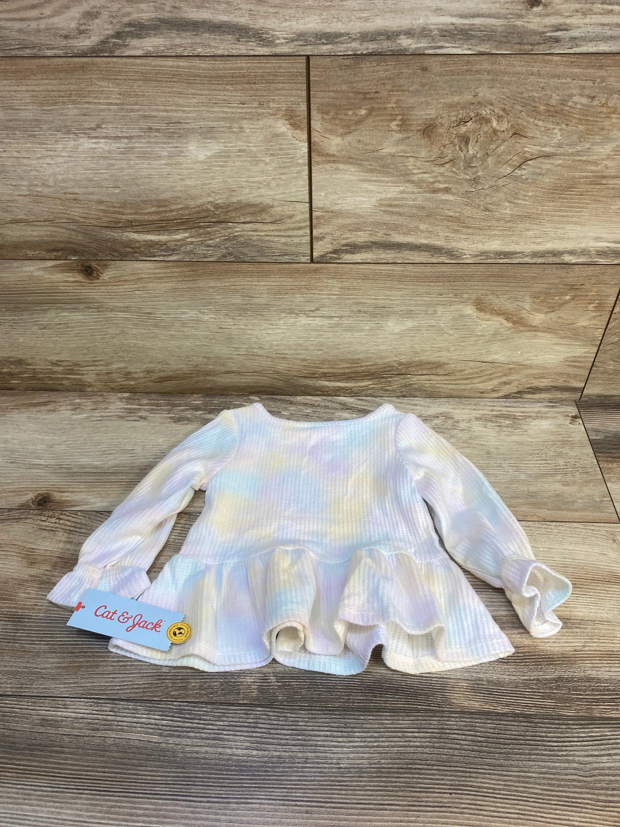 Long sleeve pastel toddler shirt with ruffle hem on wood background, Cat & Jack tag visible