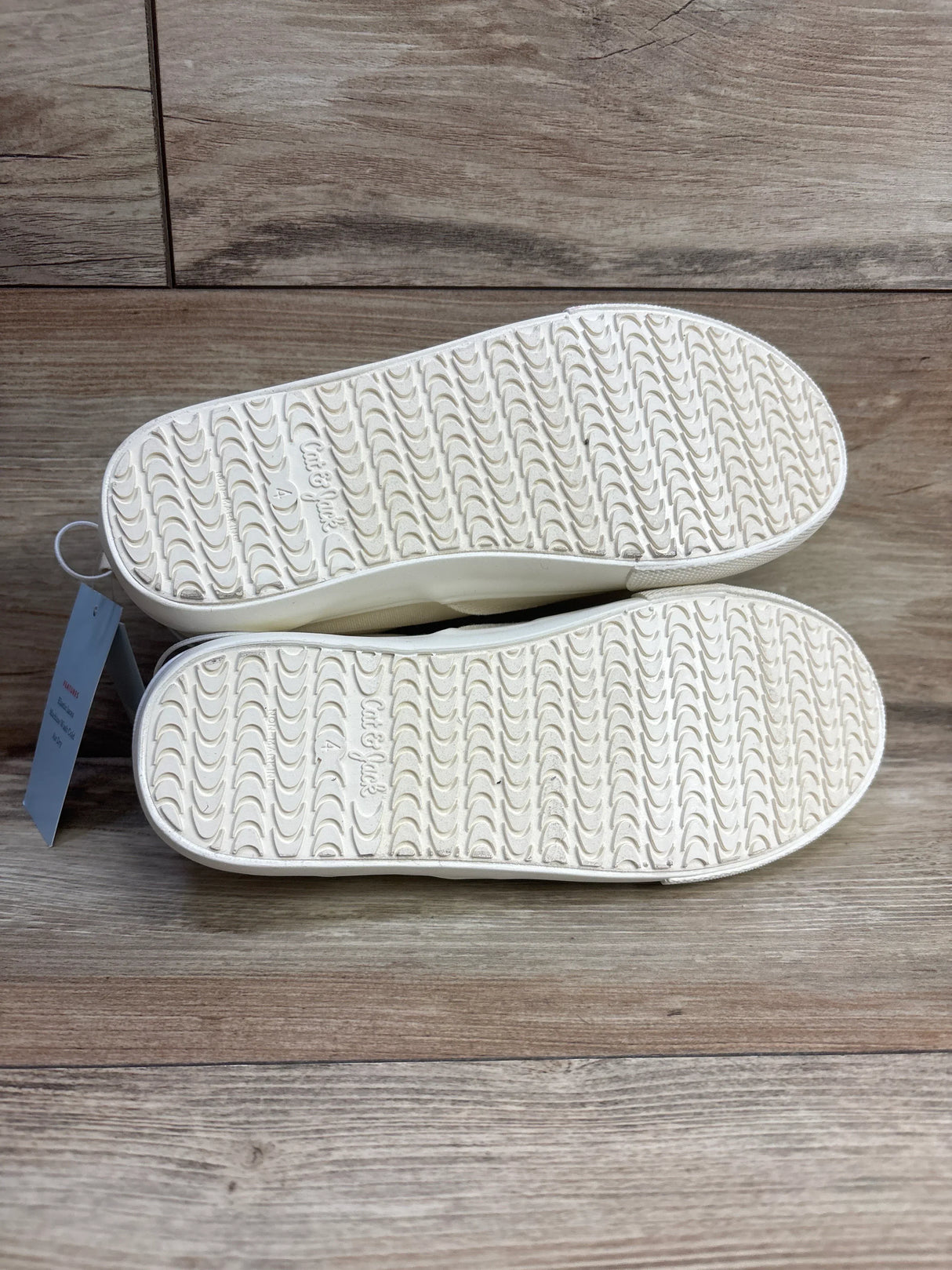 Pair of white rubber sole kids shoes with textured tread on wood floor