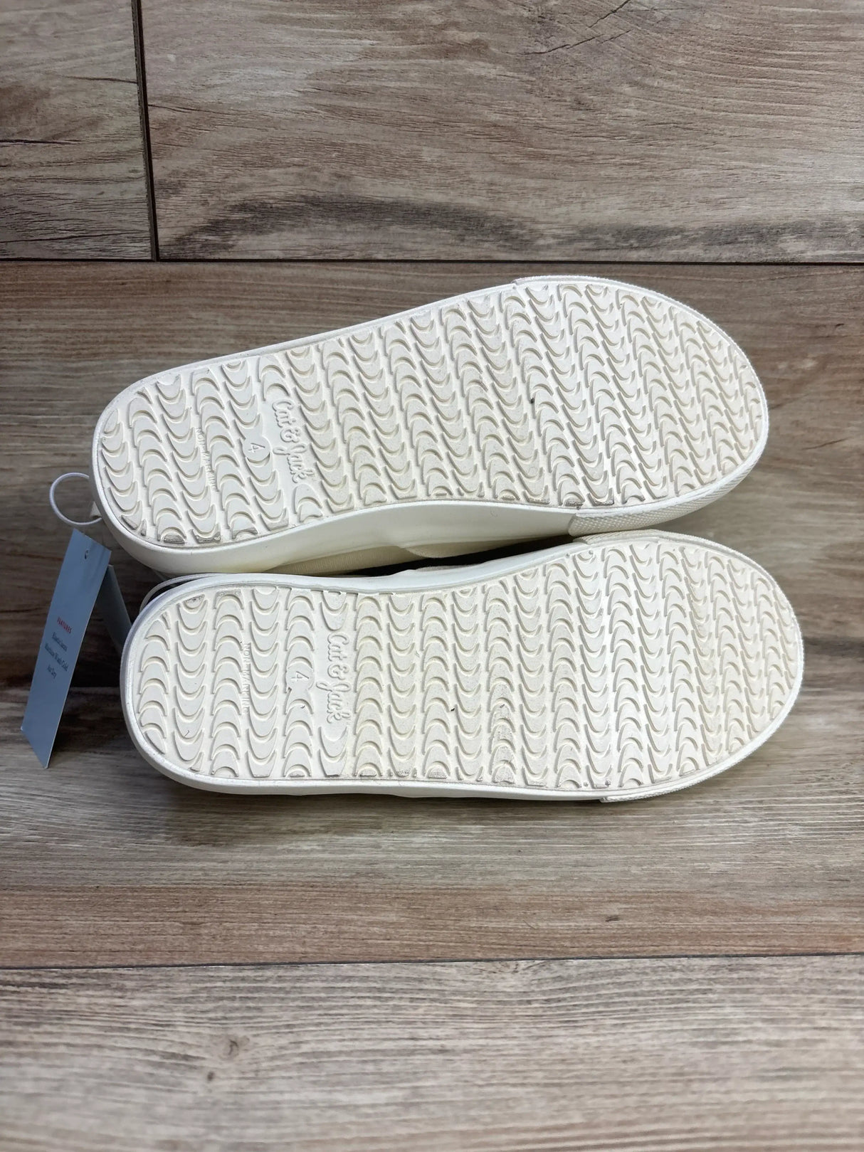 Bottom view of off-white Cat and Jack Tyler slip-on sneakers showing textured wave rubber soles on wood floor