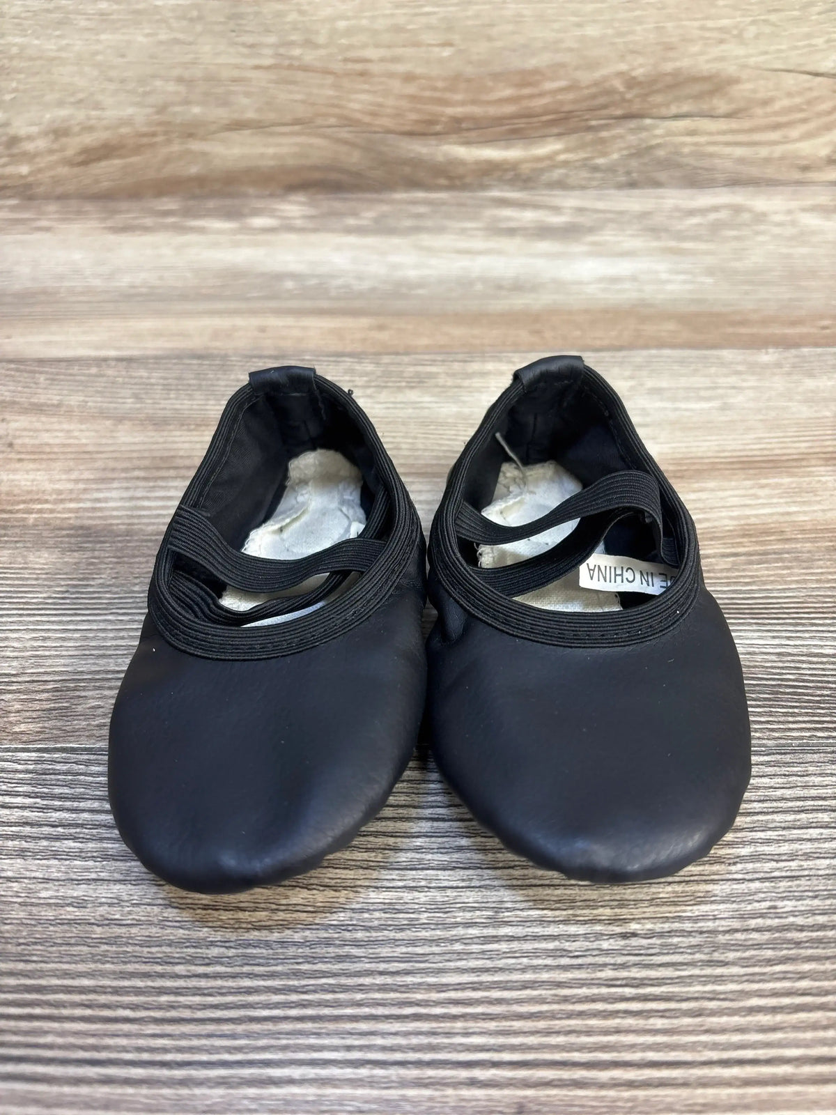 Black toddler ballet shoes with elastic straps on wooden floor