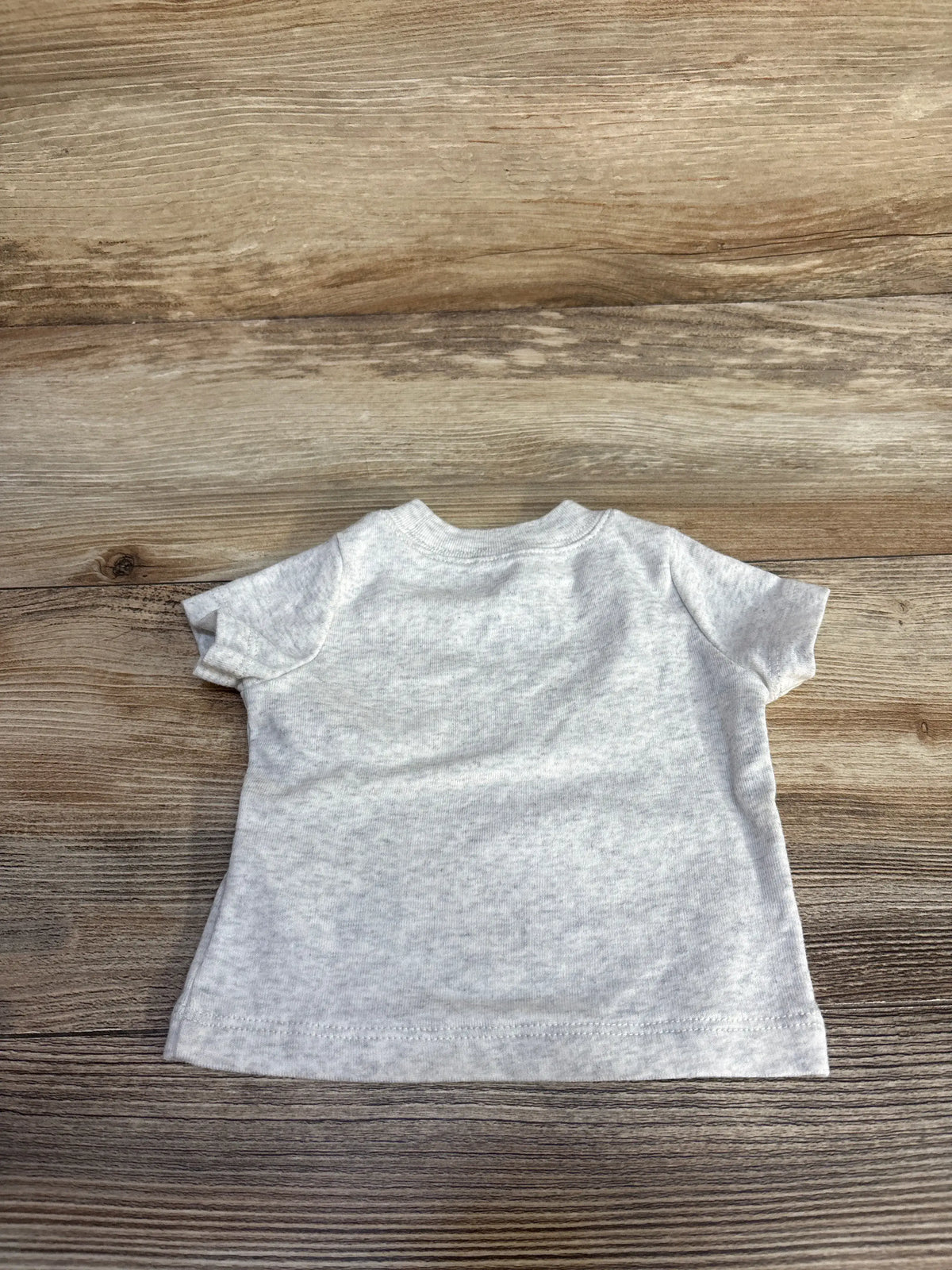 Front view of Just One You newborn shirt showcasing soft grey color, crew neckline, and relaxed fit on a wood background