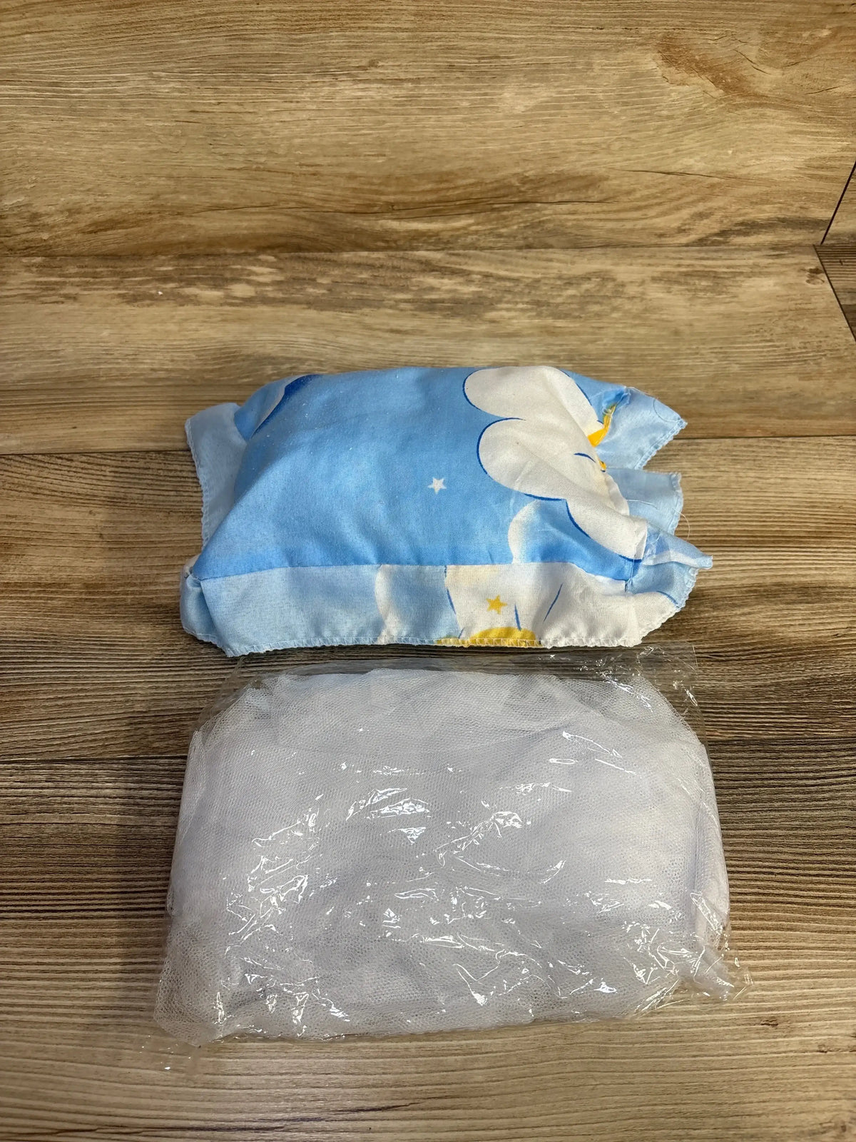 Top-down view of Care Bare Netted Nap Mat with blue cloud-print pillow and folded white mesh netting in plastic wrap on wooden floor